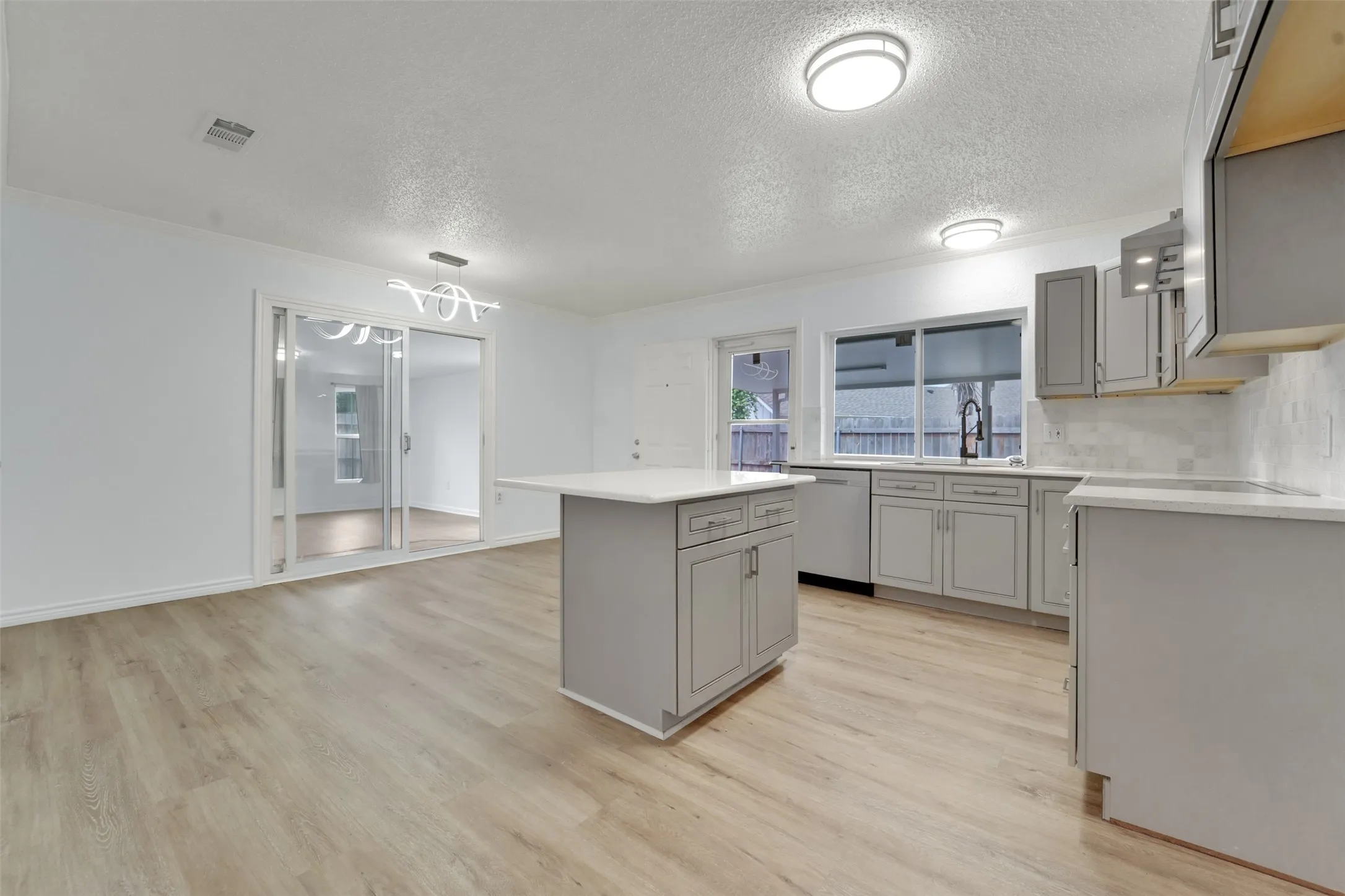 Modern kitchen featuring gray cabinetry with stainless steel appliances, a central island with prep space, quartz countertops, subway tile backsplash, recessed and pendant lighting, and wood-finish flooring throughout the open layout