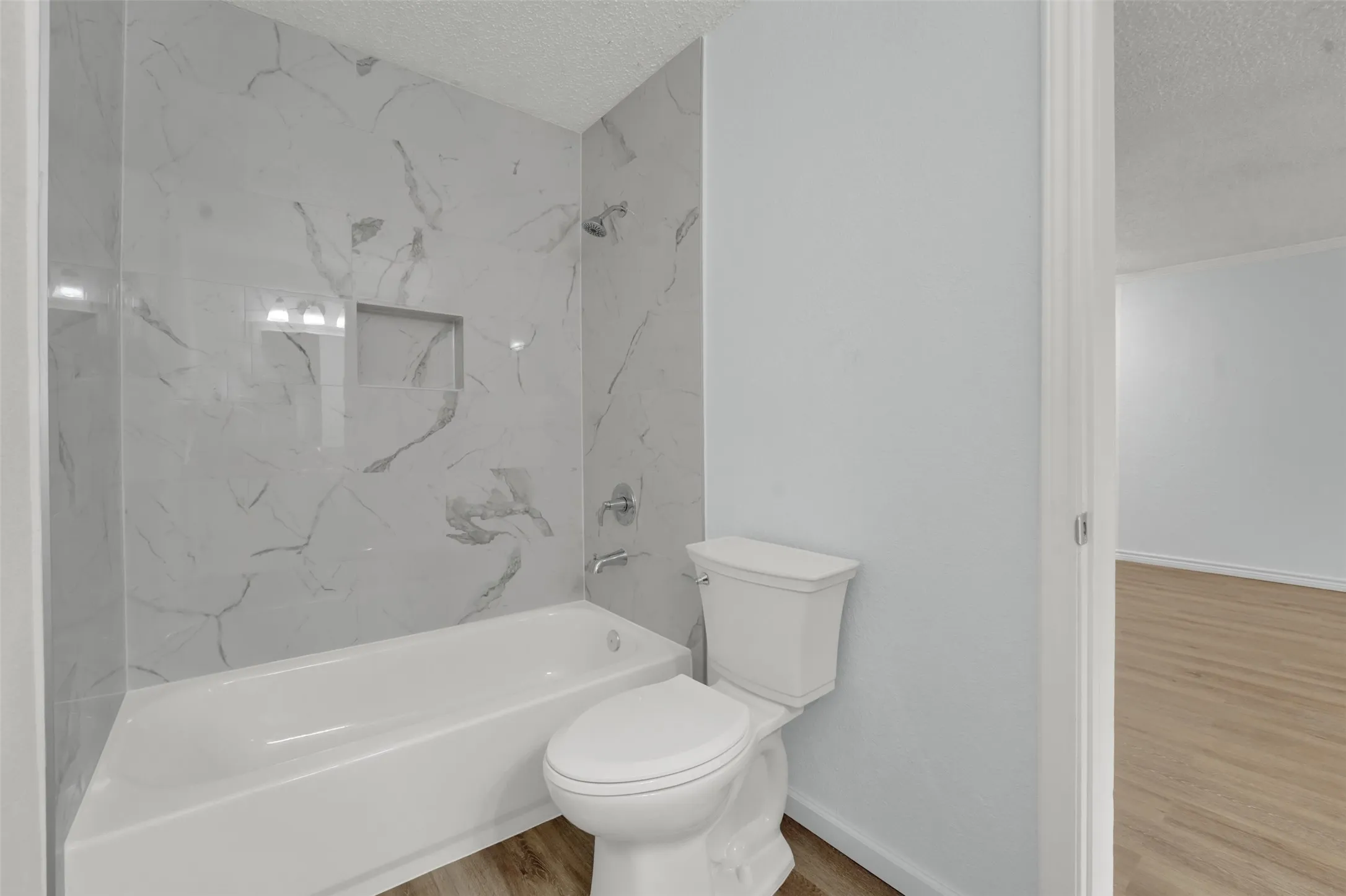 Bathtub with white marble-look tiled surround, recessed shower niche, and polished chrome fixtures