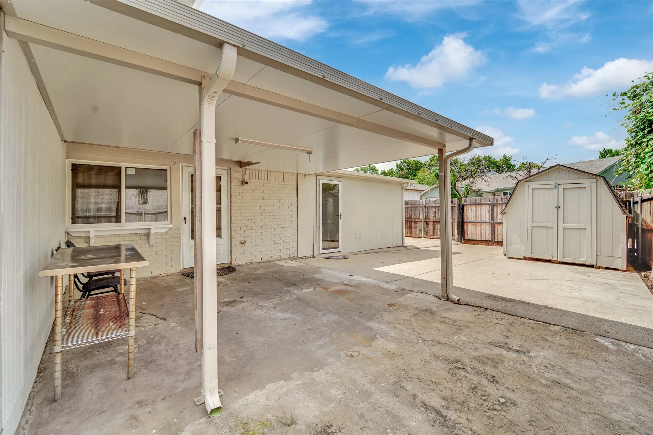 Covered patio with a concrete surface, white painted siding, and a detached storage shed