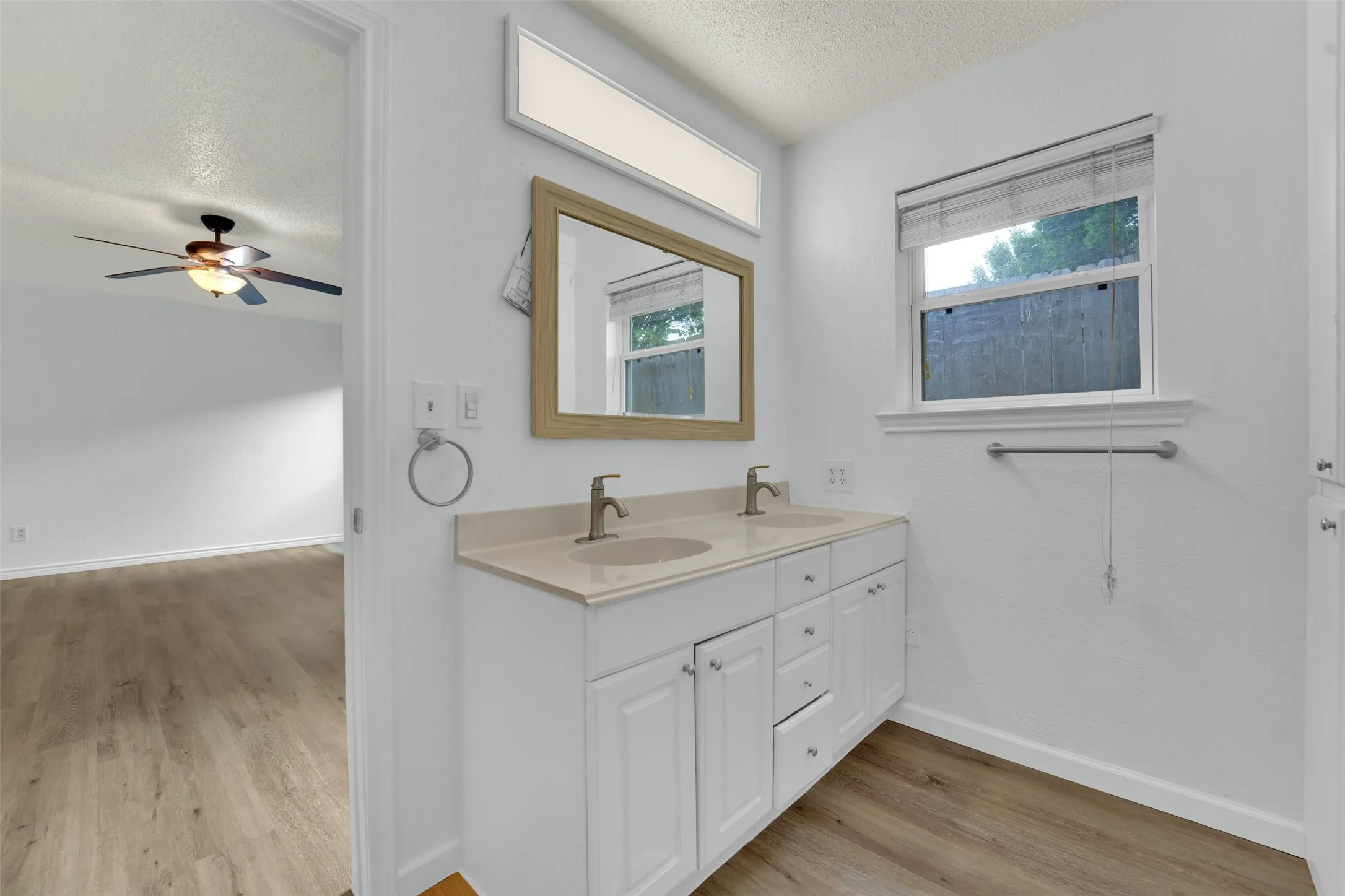 Double vanity with light-toned countertop, white cabinetry, and wood-finish flooring