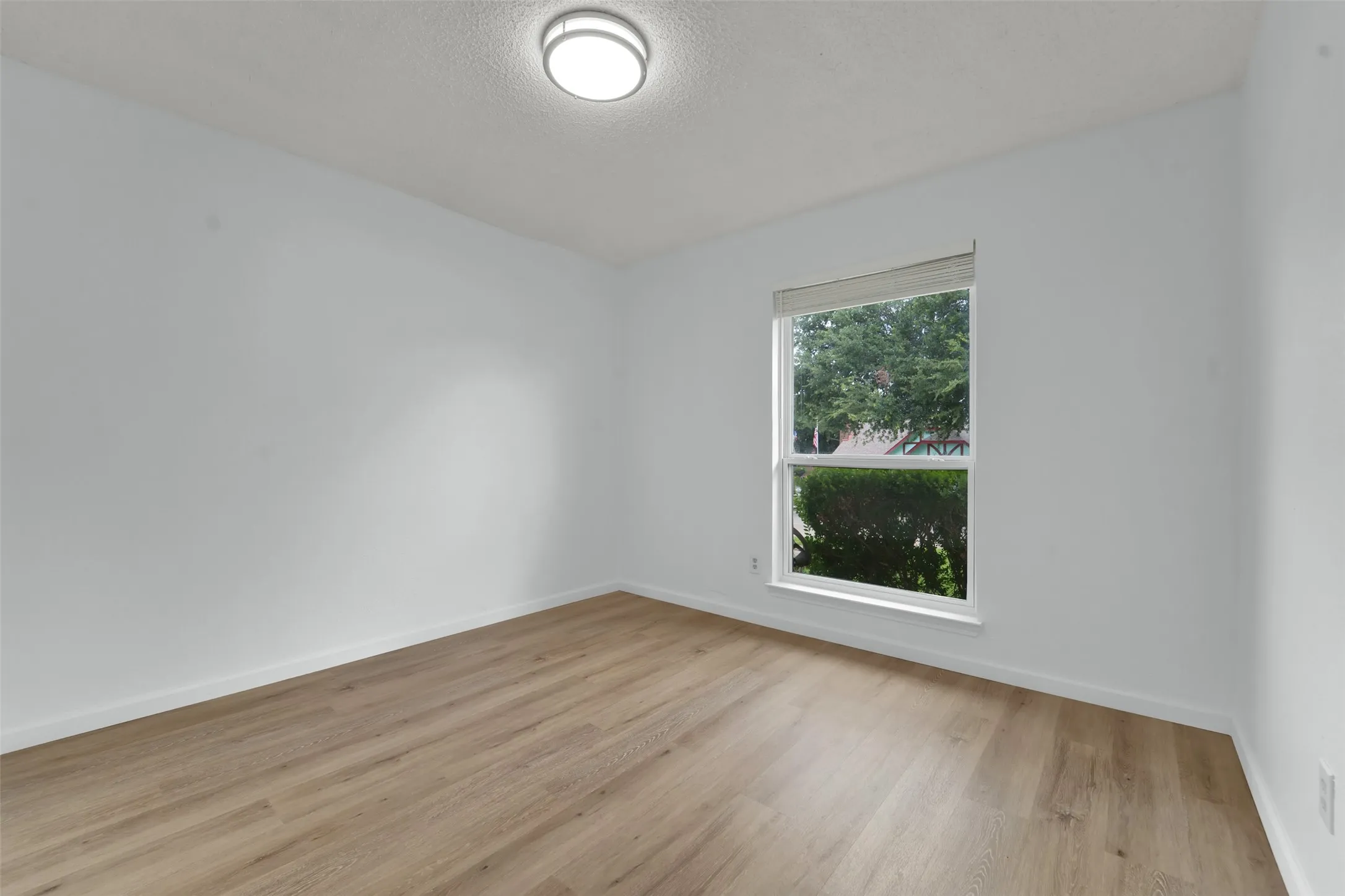 Wood-finish flooring with white baseboards, a single window, and a flush mount ceiling light fixture