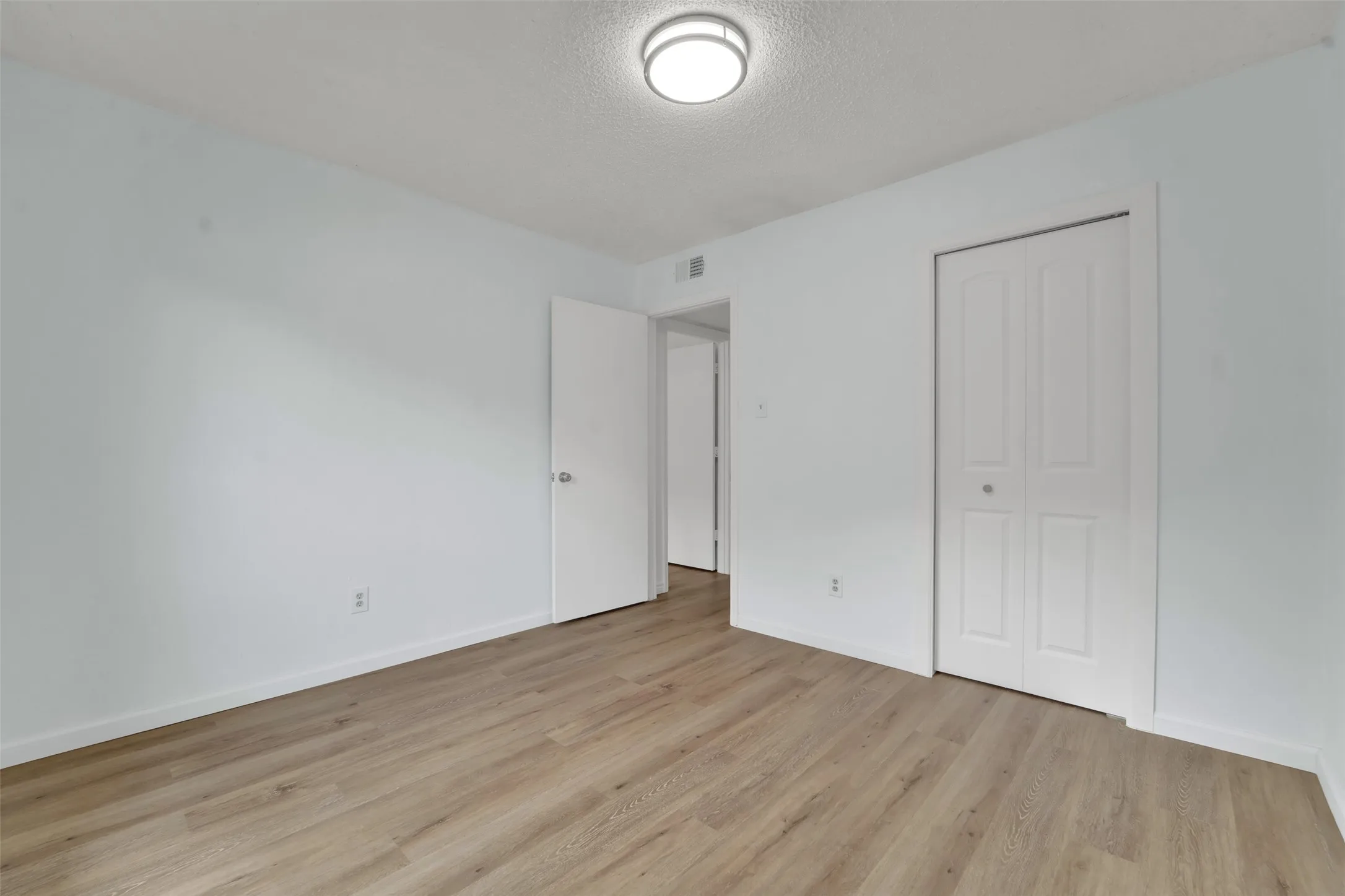 Neutral wall paint, wood-finish flooring, flush mount ceiling light, and bi-fold closet doors