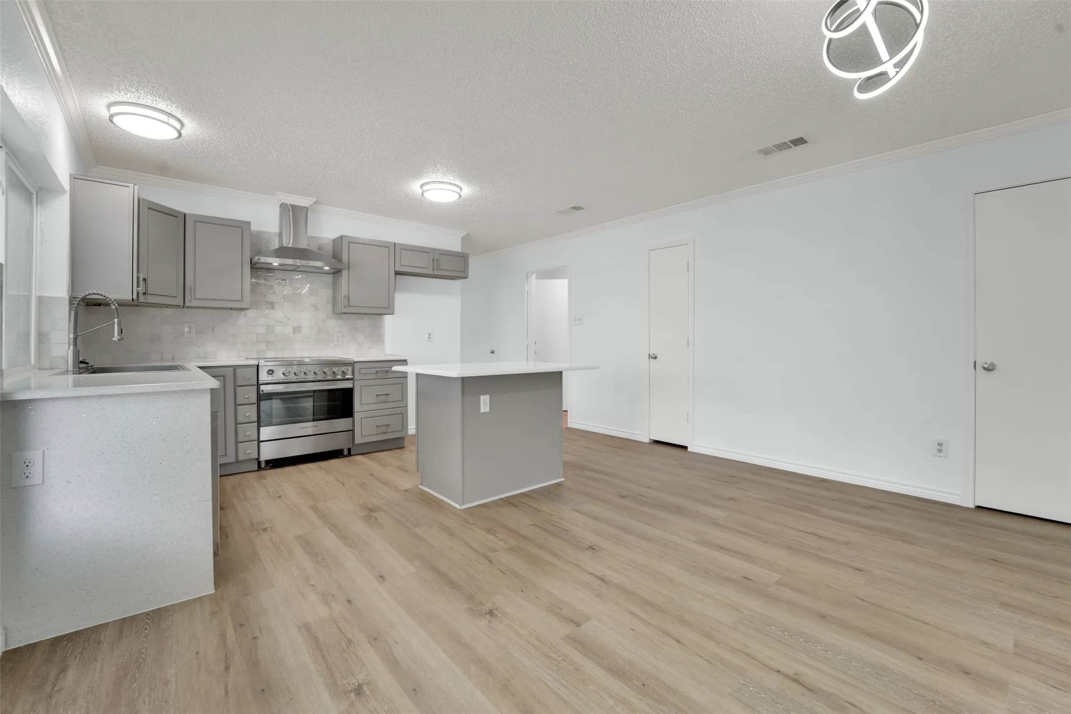 Renovated kitchen featuring gray cabinetry, stainless steel range with matching hood, subway tile backsplash, and a center island with a white countertop