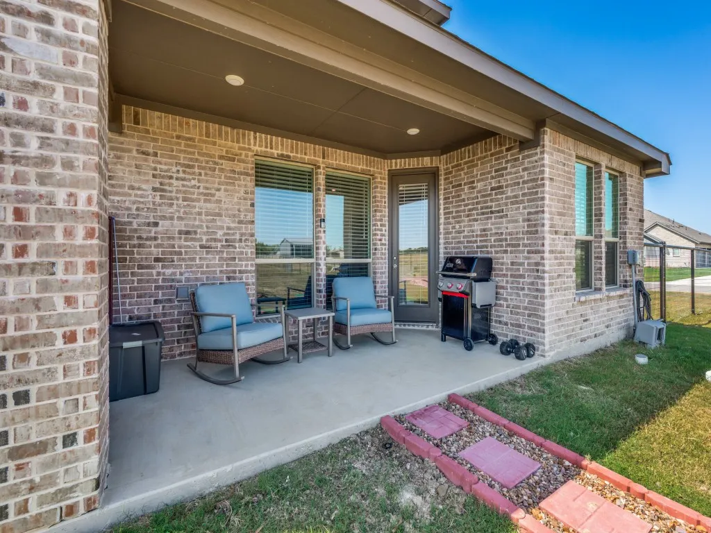 Covered outdoor patio with a concrete surface, brick exterior, and a glass-paneled door