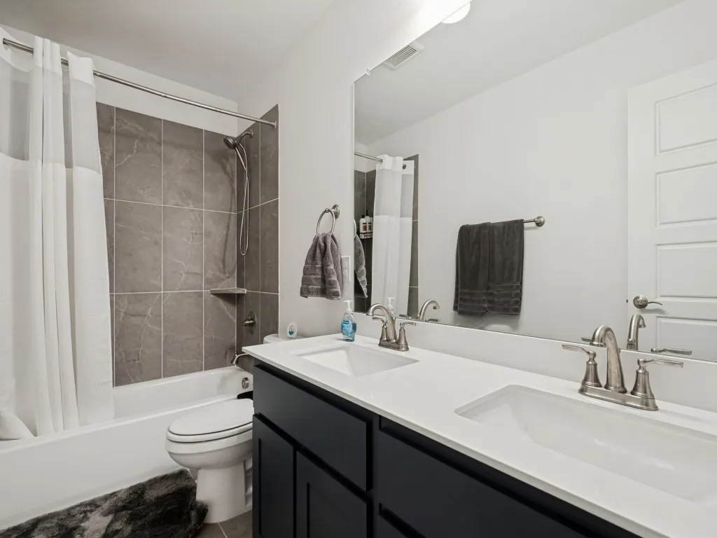 Bathroom featuring a dual vanity with white countertops, brushed nickel fixtures, a tub with a shower, and gray wall tile