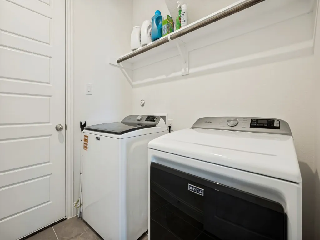 Utility area with overhead shelving, wood-finish hanging rod, and tiled flooring