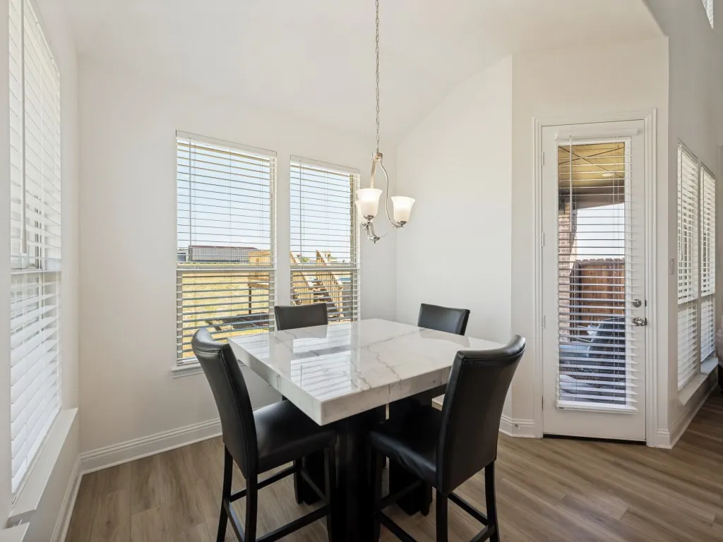 Vaulted ceiling, wood-finish flooring, multiple windows with blinds, and a door with blinds