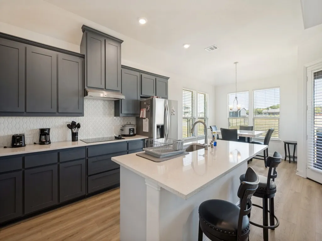 Kitchen featuring dark shaker-style cabinetry, light countertops, wood-finish flooring, a kitchen island with sink, and a built-in cooktop