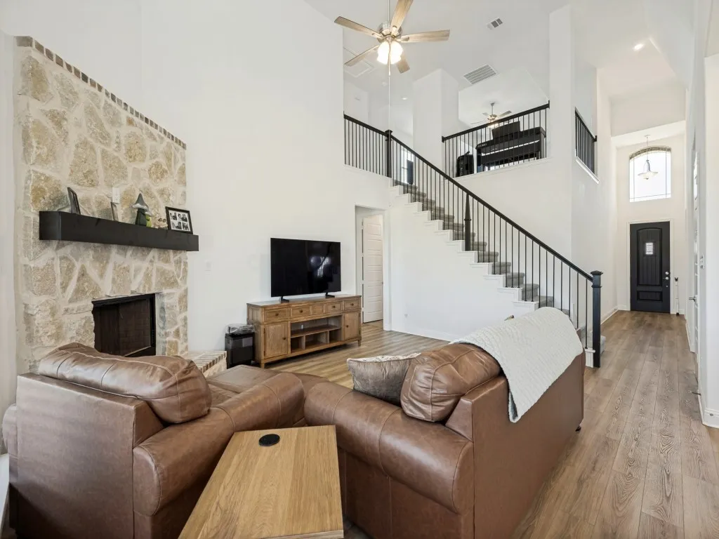 Vaulted ceiling living space with a stone fireplace, wood-finish flooring, and a staircase featuring wrought iron balusters