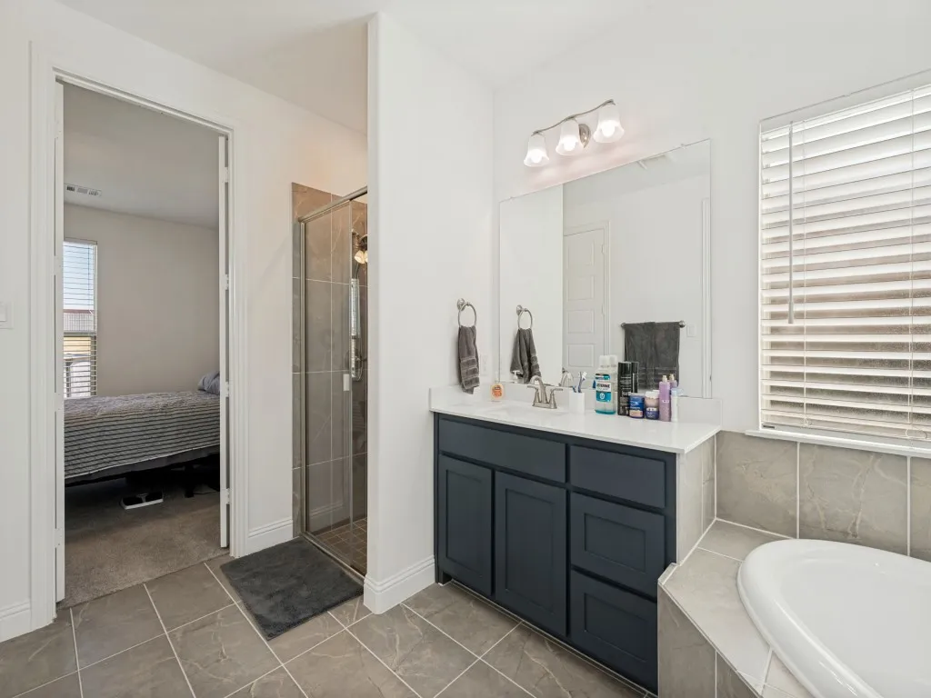 Primary bathroom featuring a built-in soaking tub, glass-enclosed shower, single vanity with a white countertop, and tiled flooring