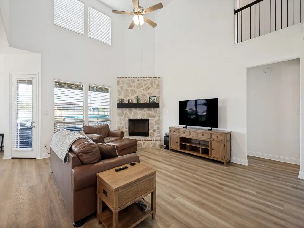 Two-story living area featuring a stone-clad corner fireplace with a dark mantel, wood-finish flooring, and a ceiling fan