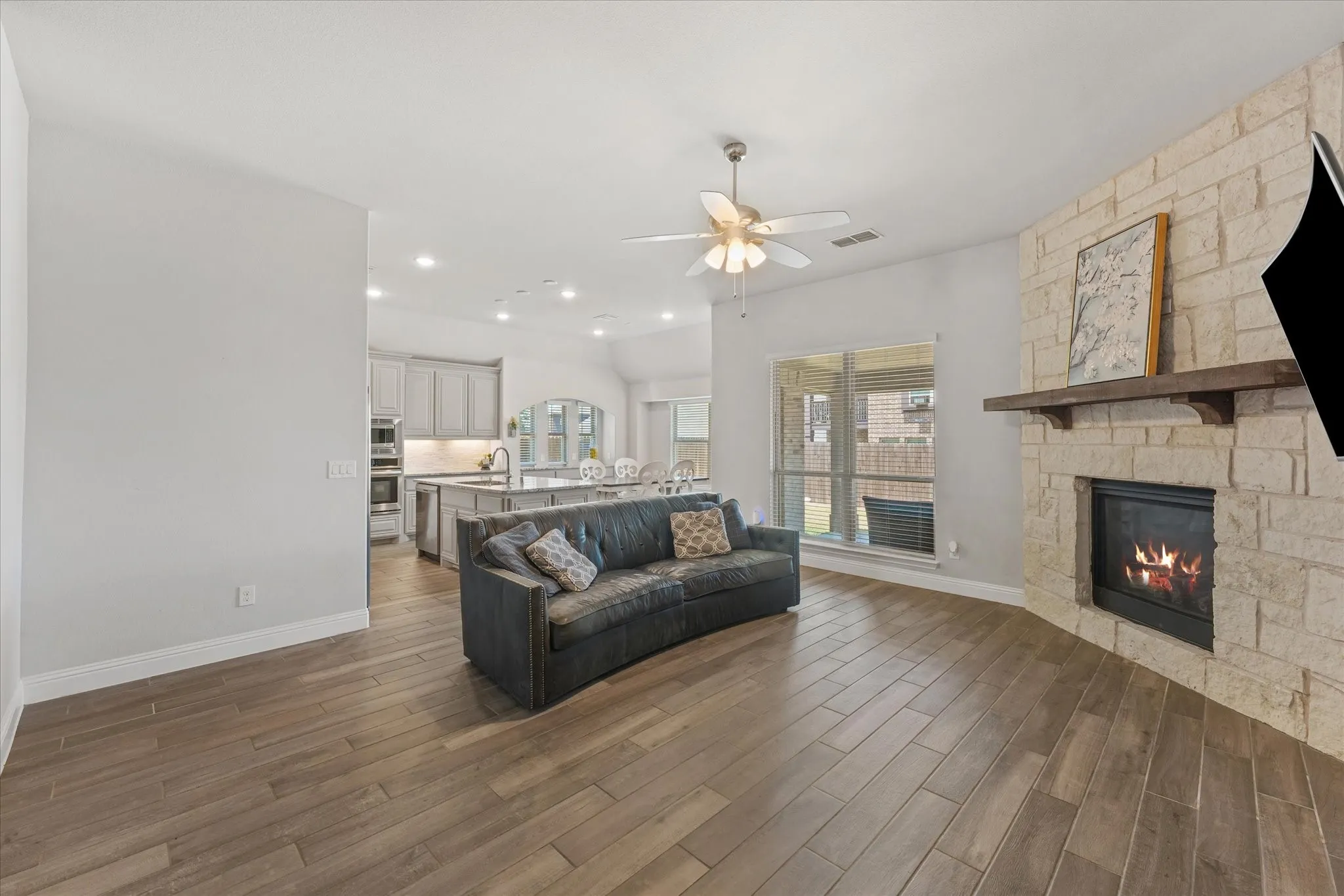 Open-concept living - spacious living area with a beautiful stone fireplace with wood mantel, abundant natural light, and seamless flow into the chef's dream kitchen.