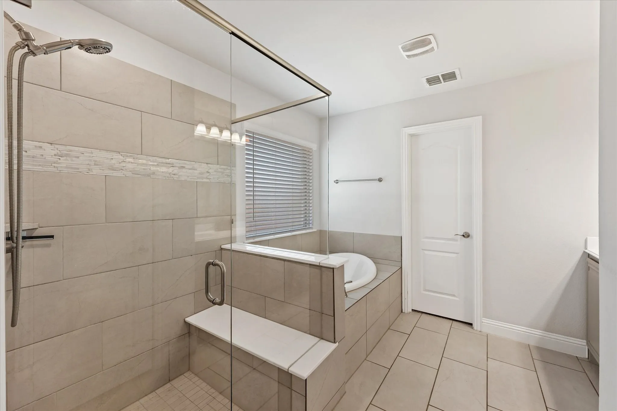 Glass-enclosed shower with a built-in bench, tiled walls featuring a decorative accent band, and a separate soaking tub