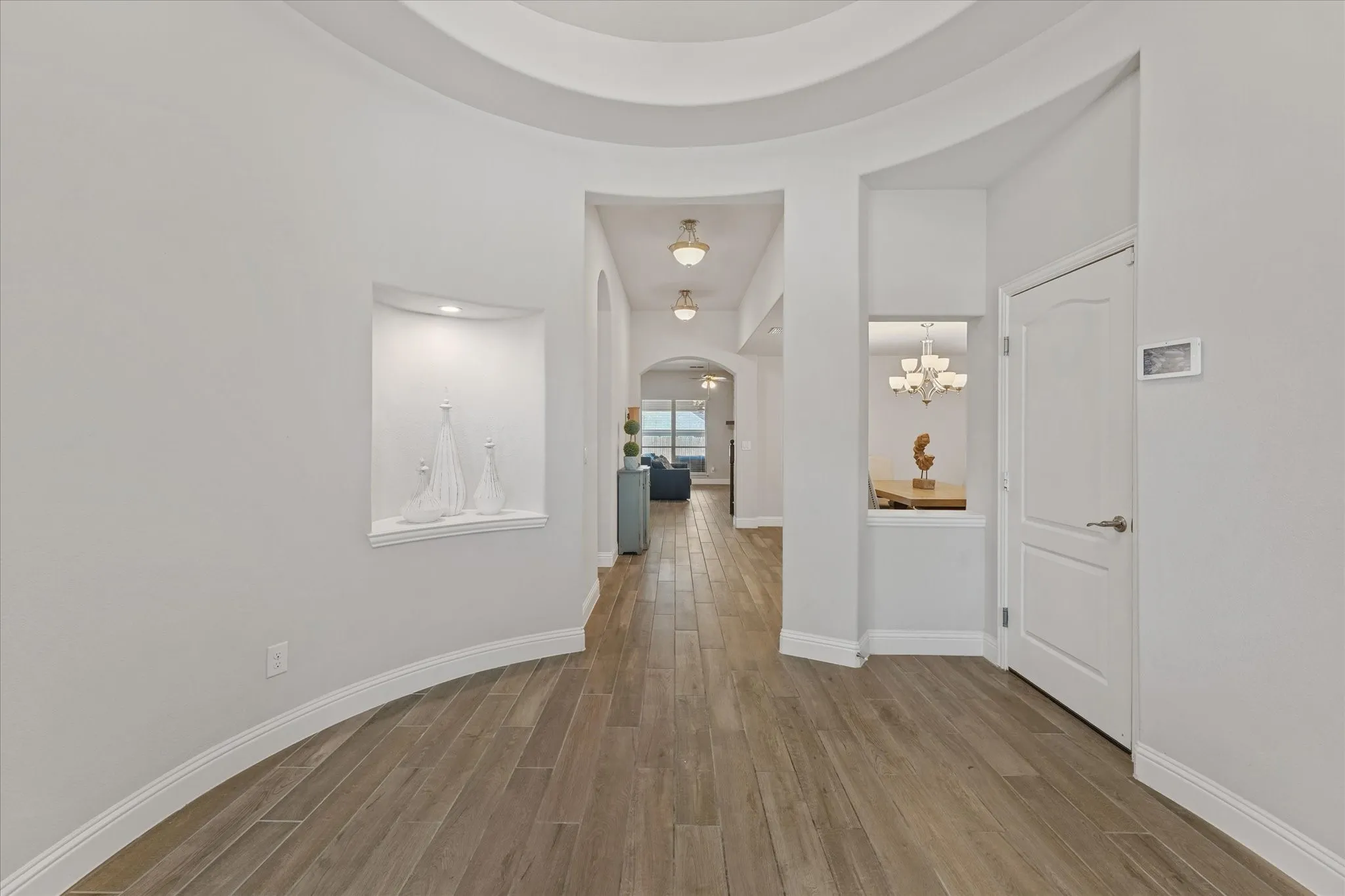 Light-filled foyer with graceful arches, decorative niches, and warm wood-look tile plank flooring flowing throughout.