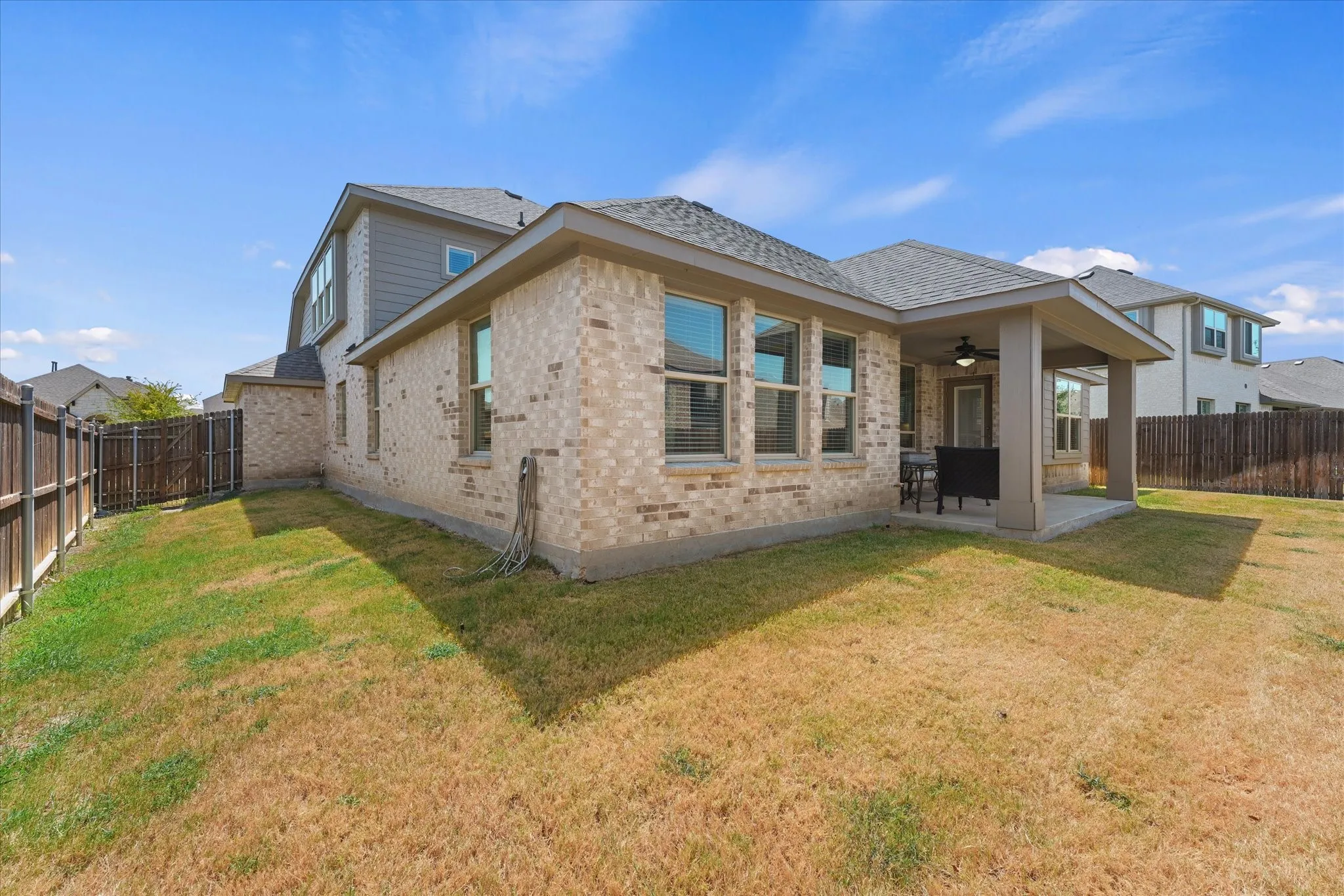 Brick exterior with multiple windows, covered patio, and fenced perimeter