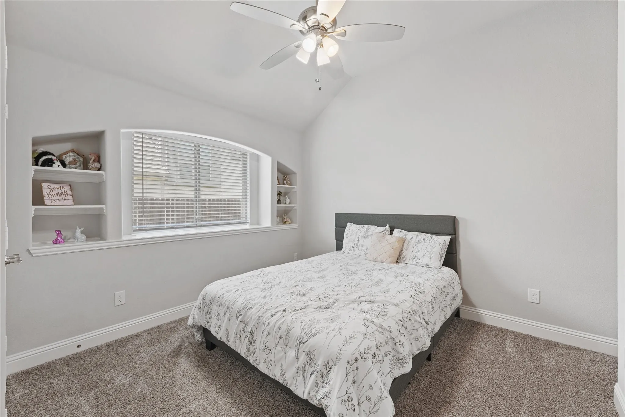 Vaulted ceiling with a ceiling fan, arched window with blinds, and built-in wall shelving