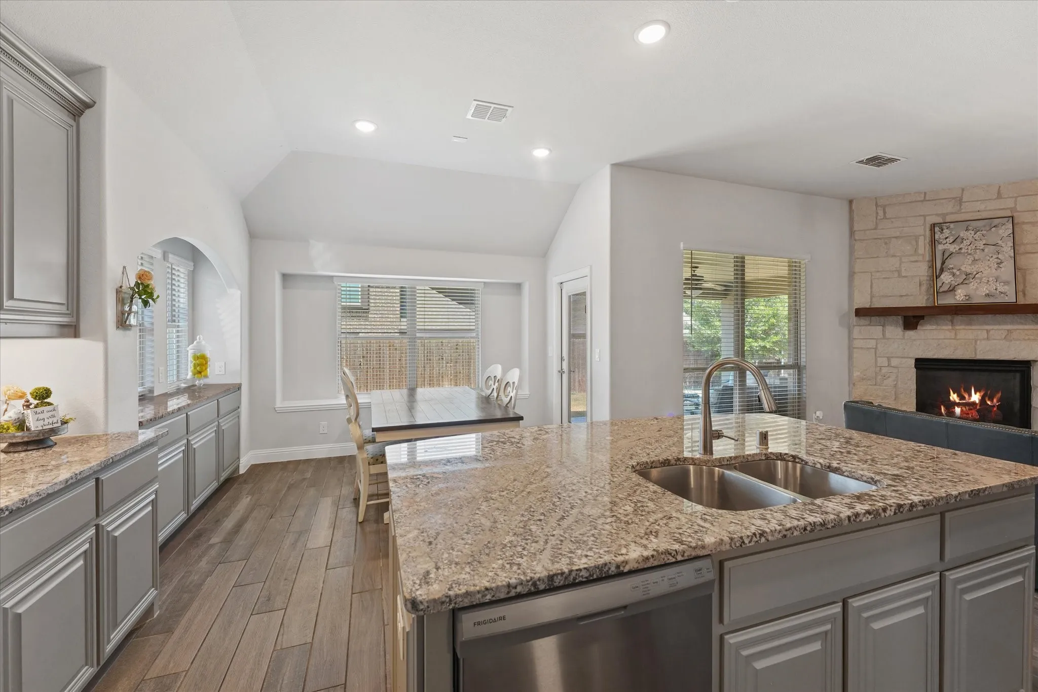 Spacious kitchen island with integrated stainless steel sink, wood-look flooring, recessed lighting, fireplace with stone surround, and wood mantel