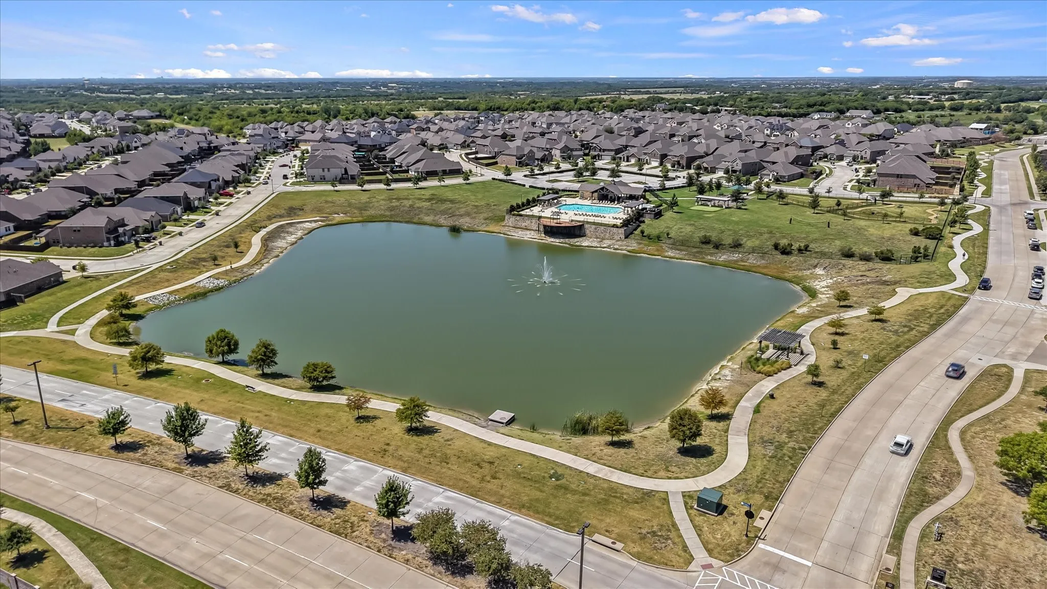 Community lake with a water feature, paved walking paths, and a swimming pool across from elementary school.
