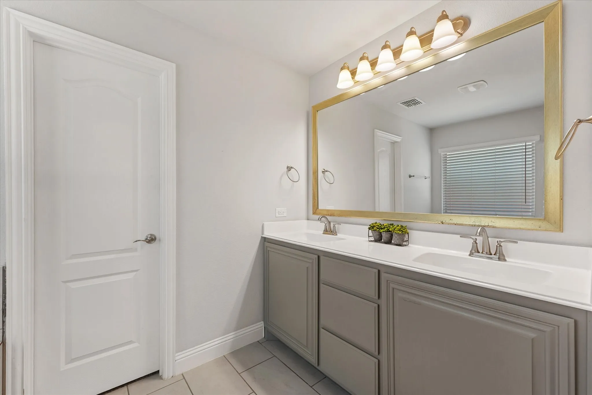 Dual vanity with integrated sinks and brushed nickel faucets, set below a large framed mirror with overhead lighting