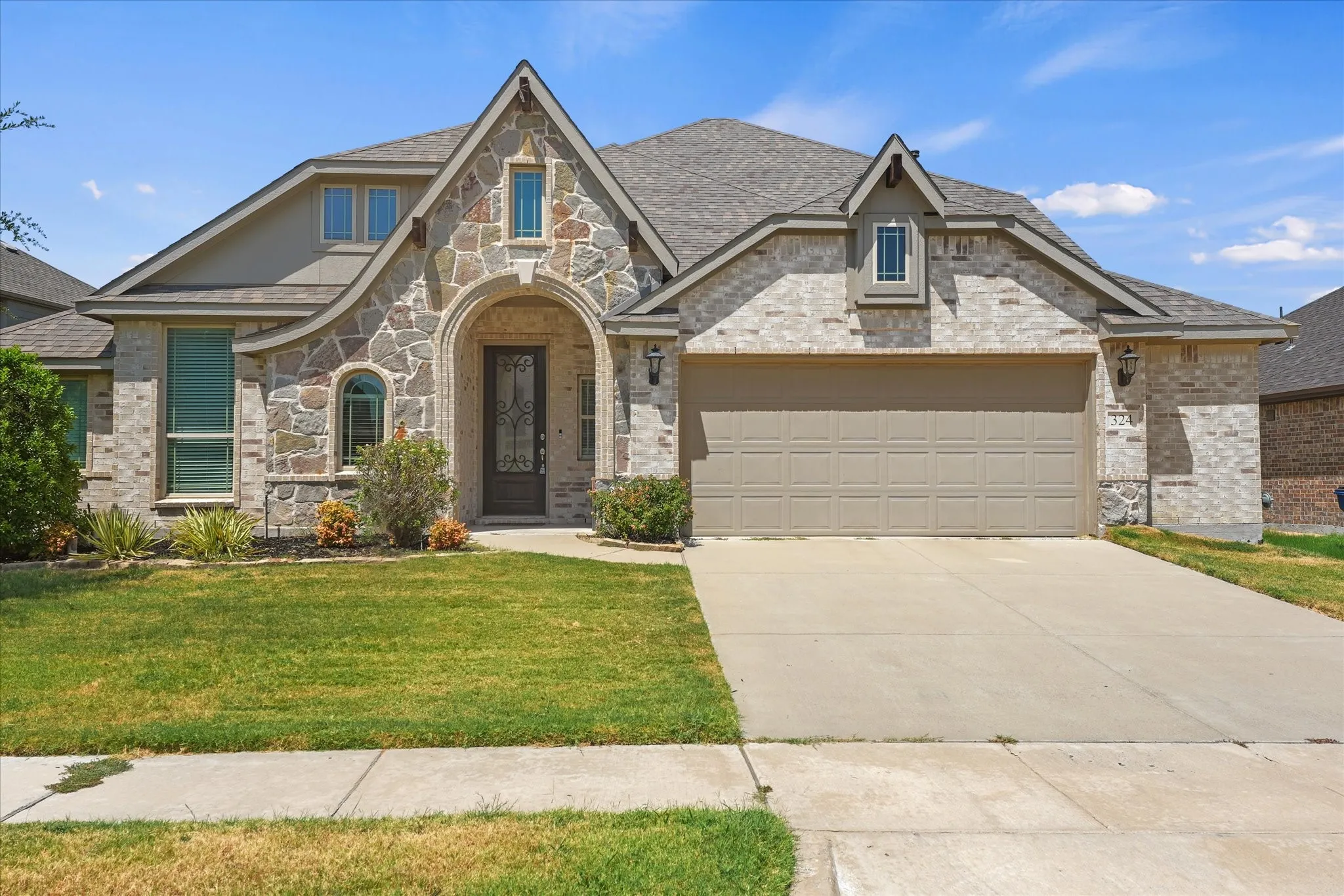 Stone and brick facade with an arched entry, prominent gable, a two-car garage, and a landscaped front yard