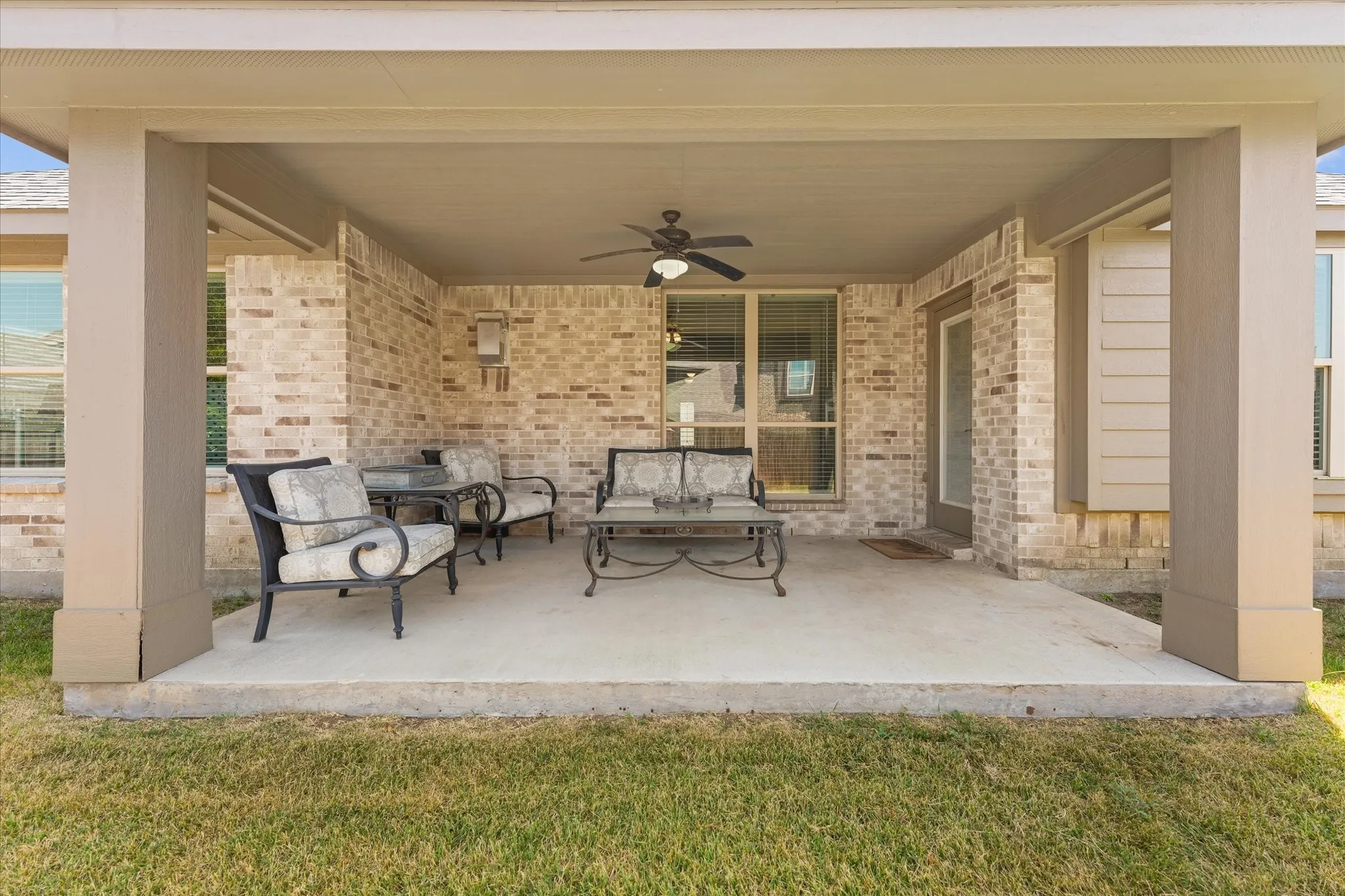 Large covered patio ready for outdoor entertainment and relaxation with a concrete slab, brick exterior, and a ceiling fan