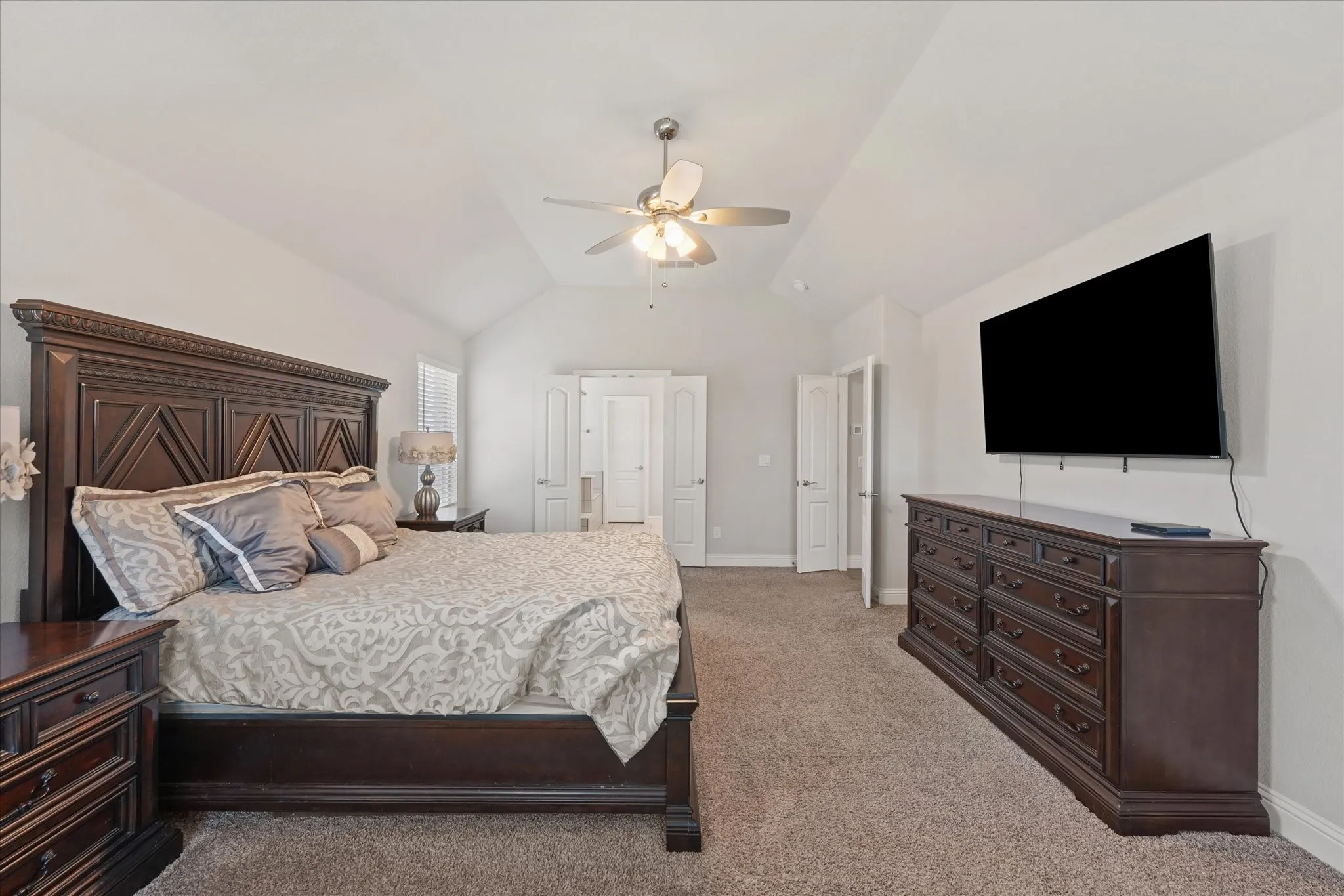 Generously sized primary bedroom with vaulted ceiling, plush carpeting, ceiling fan, and French doors leading to the primary bath.