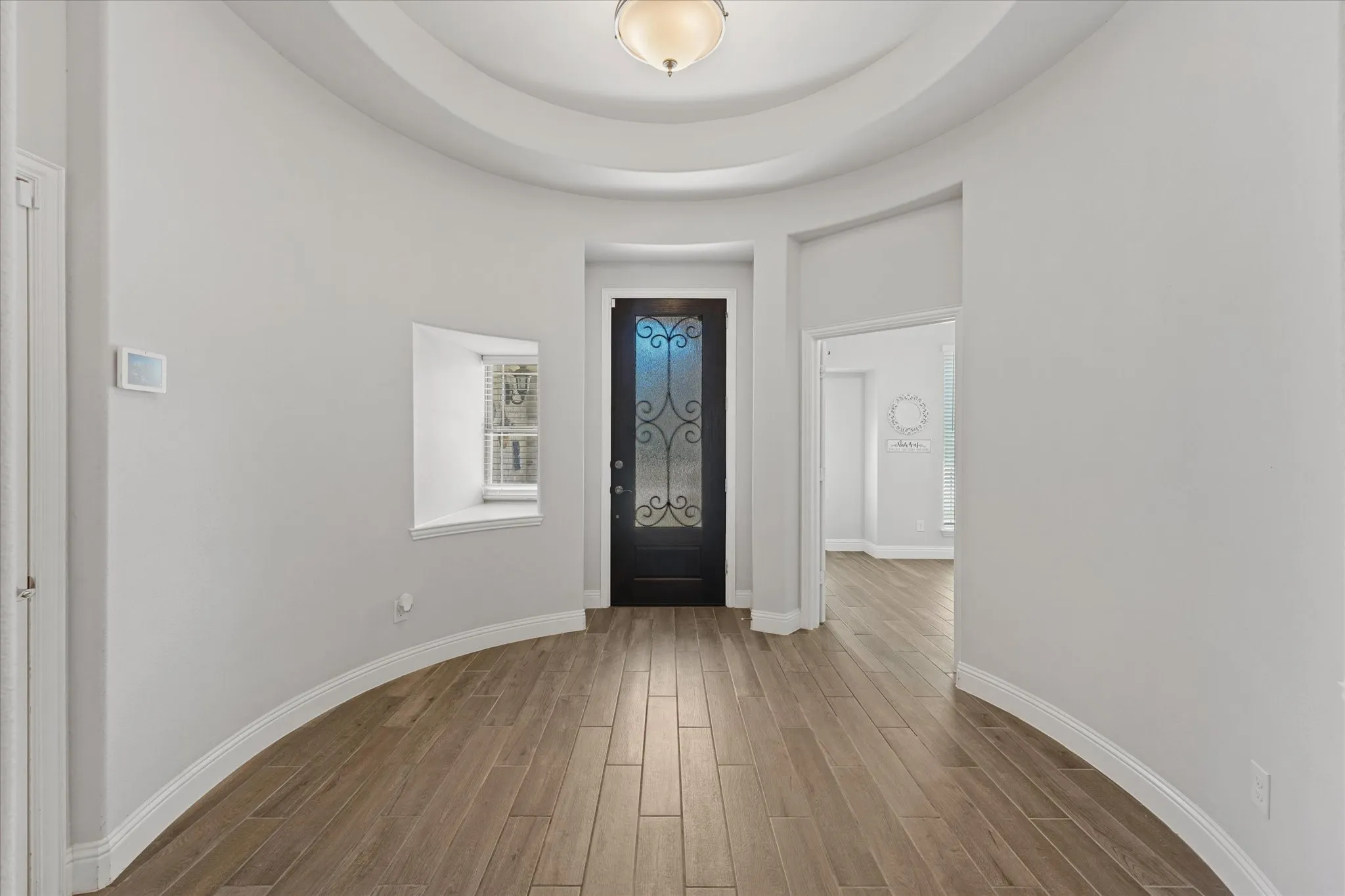 Beautiful curved entryway with tray ceiling, wood-look tile plank flooring, and a decorative frosted glass entry door