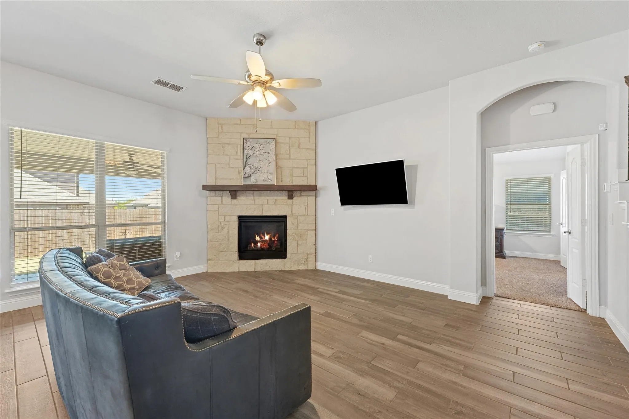 Bright, inviting living space with a stone fireplace, wood mantel, abundant natural light, and warm wood-look flooring.
