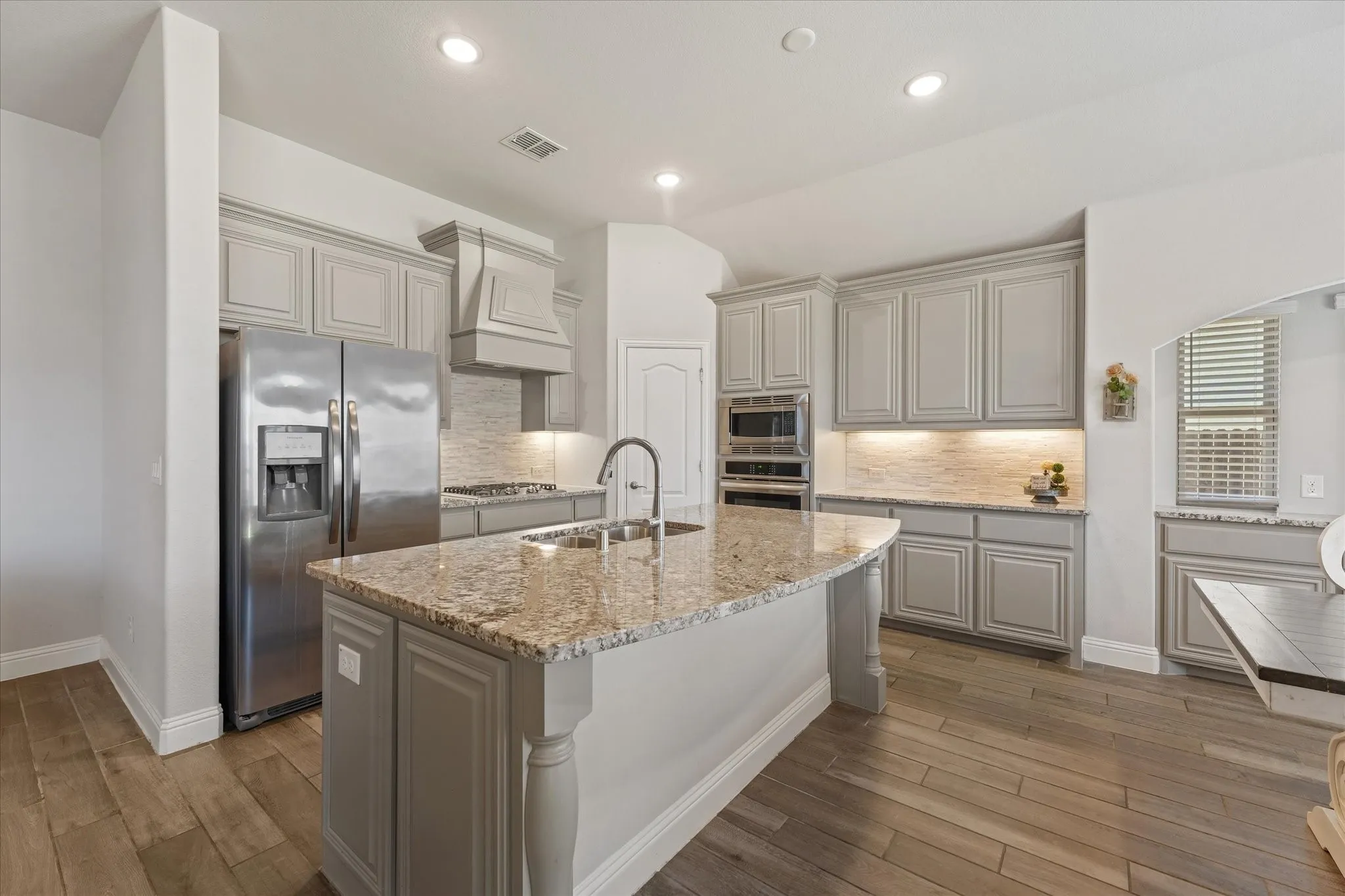 Elegant kitchen featuring granite countertops, extensive cabinetry, recessed lighting, and a striking custom vented range hood.