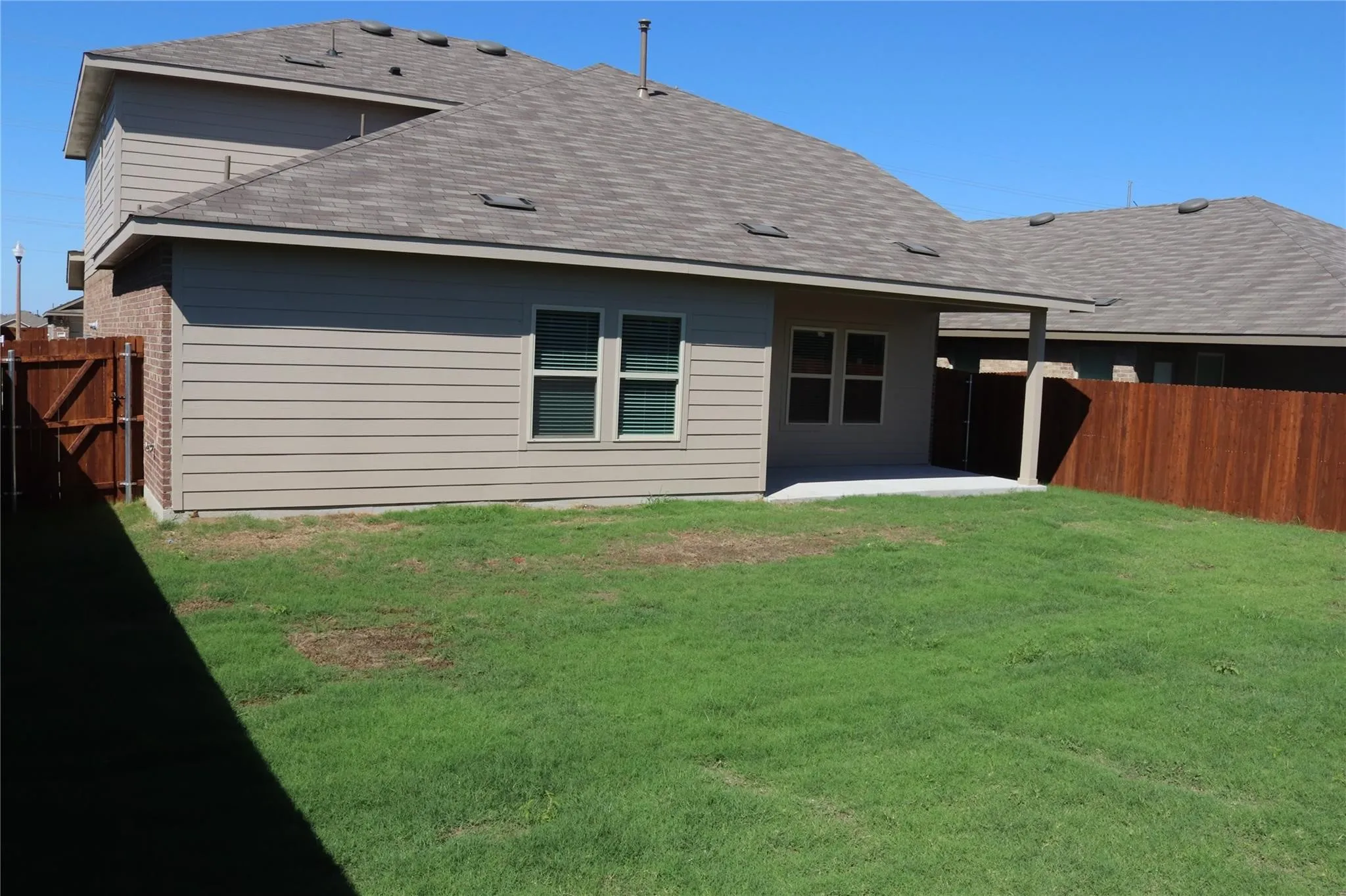 Expansive backyard with a covered patio, wood fencing, and a manicured lawn