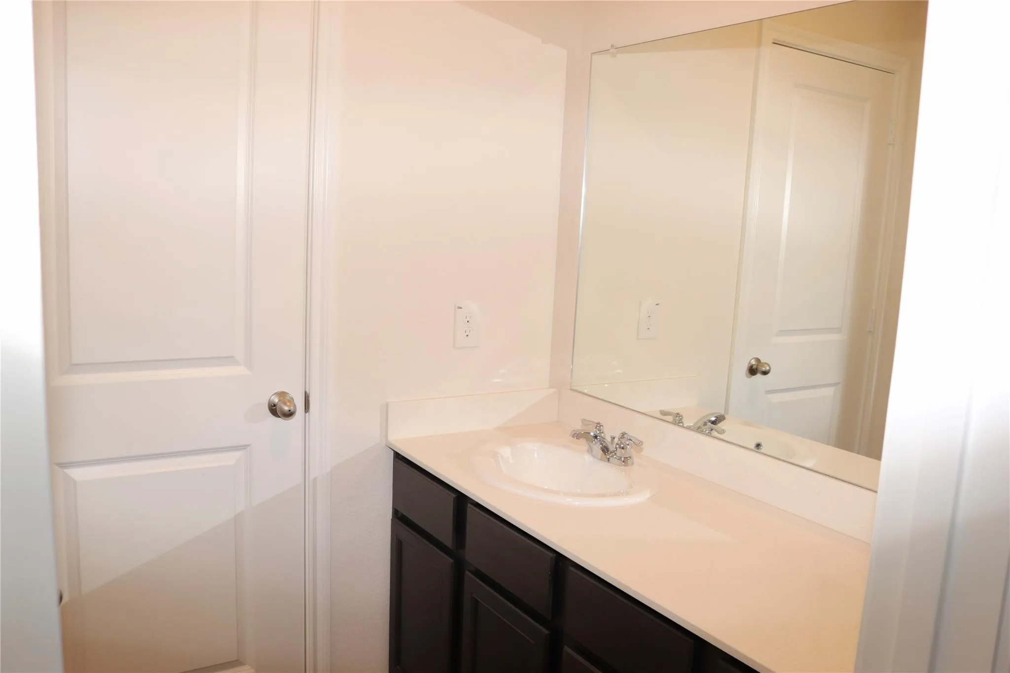 Dark wood-finish vanity with a white countertop and integrated sink, chrome faucet fixtures, and a large wall-mounted mirror