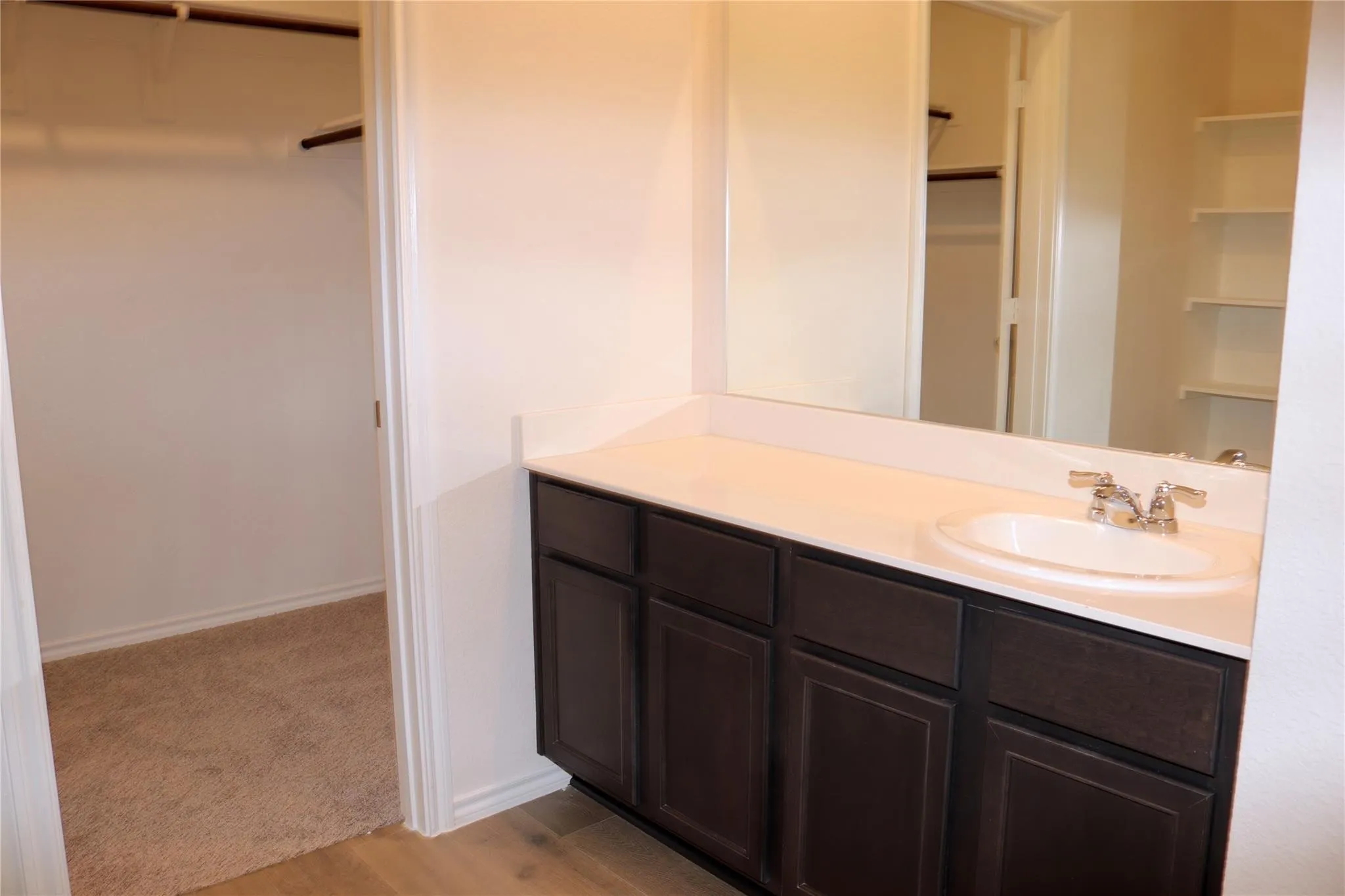 Vanity with dark wood-finish cabinetry, white countertop, and integrated sink