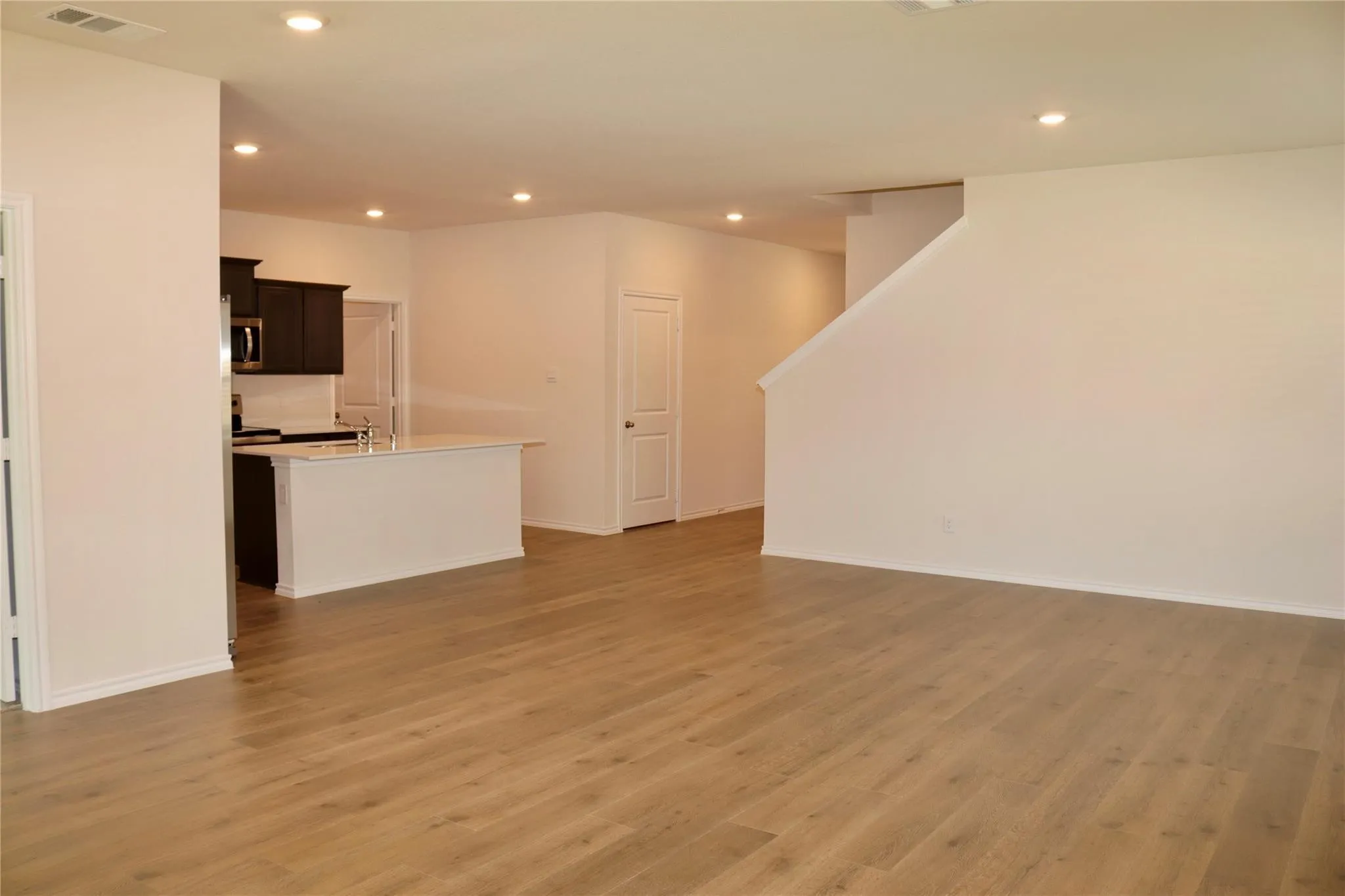 Open-concept living area with wood-finish flooring, recessed lighting, and a kitchen island with a built-in sink