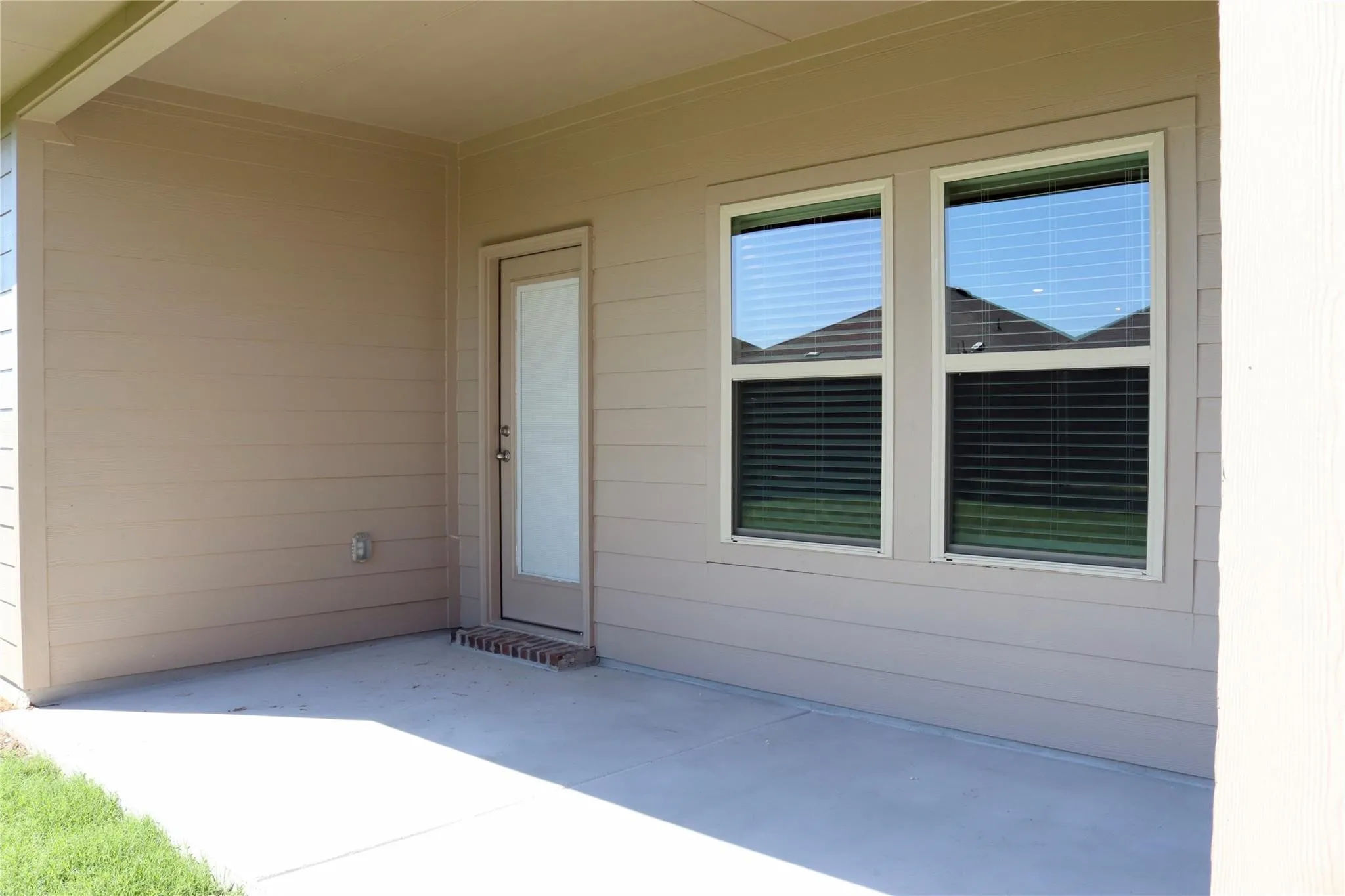 Covered concrete patio with siding exterior, privacy door, and dual windows