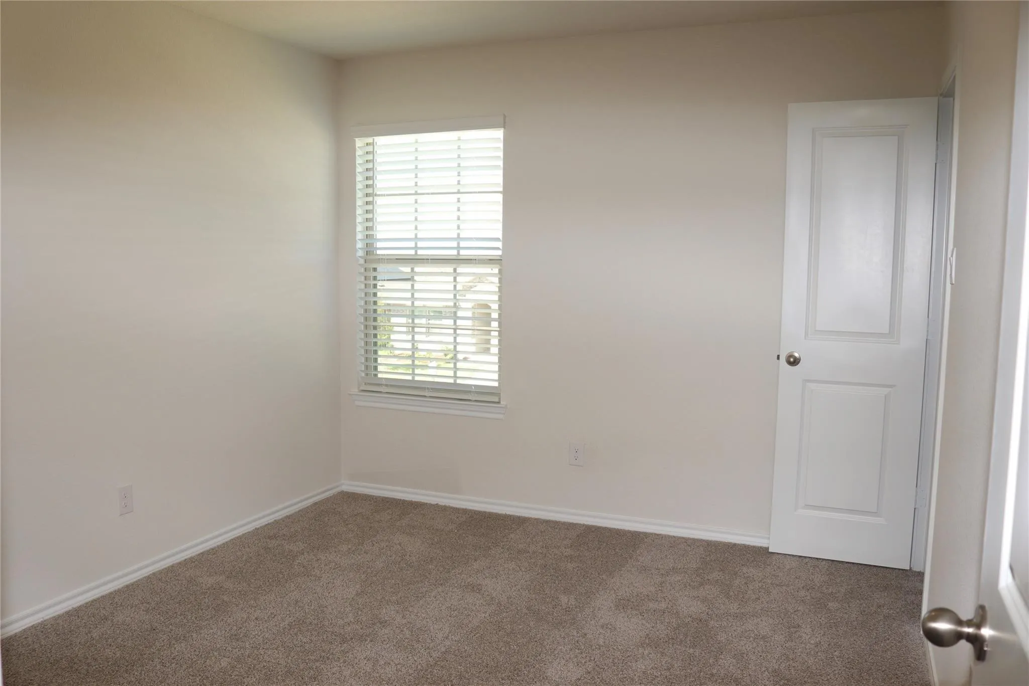 Neutral wall paint, carpeted flooring, window with blinds, panel door, and brushed nickel hardware
