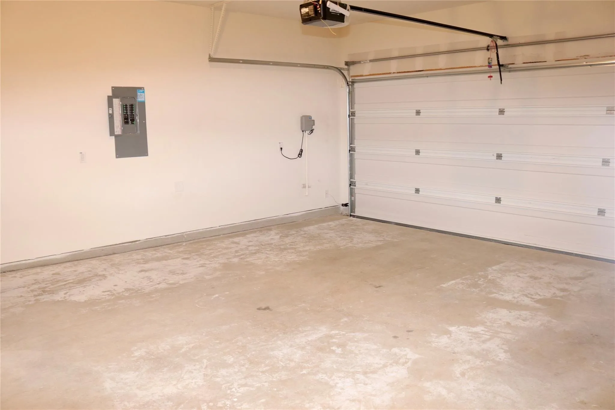 Garage space featuring a paneled overhead door, concrete flooring, and an exposed electrical panel