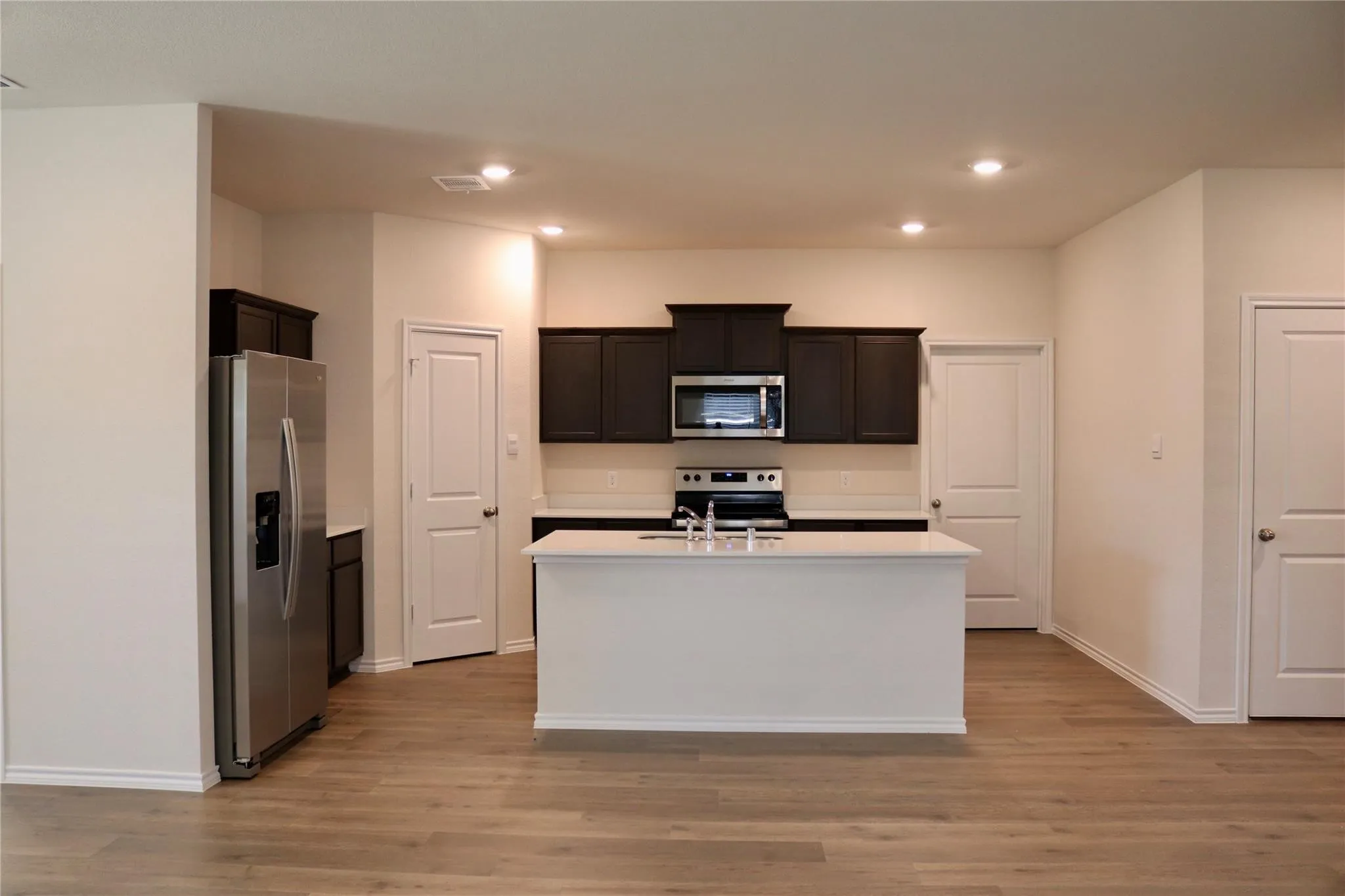 Kitchen featuring dark wood cabinetry, stainless steel appliances, a center island with a sink, recessed lighting, and wood-finish flooring