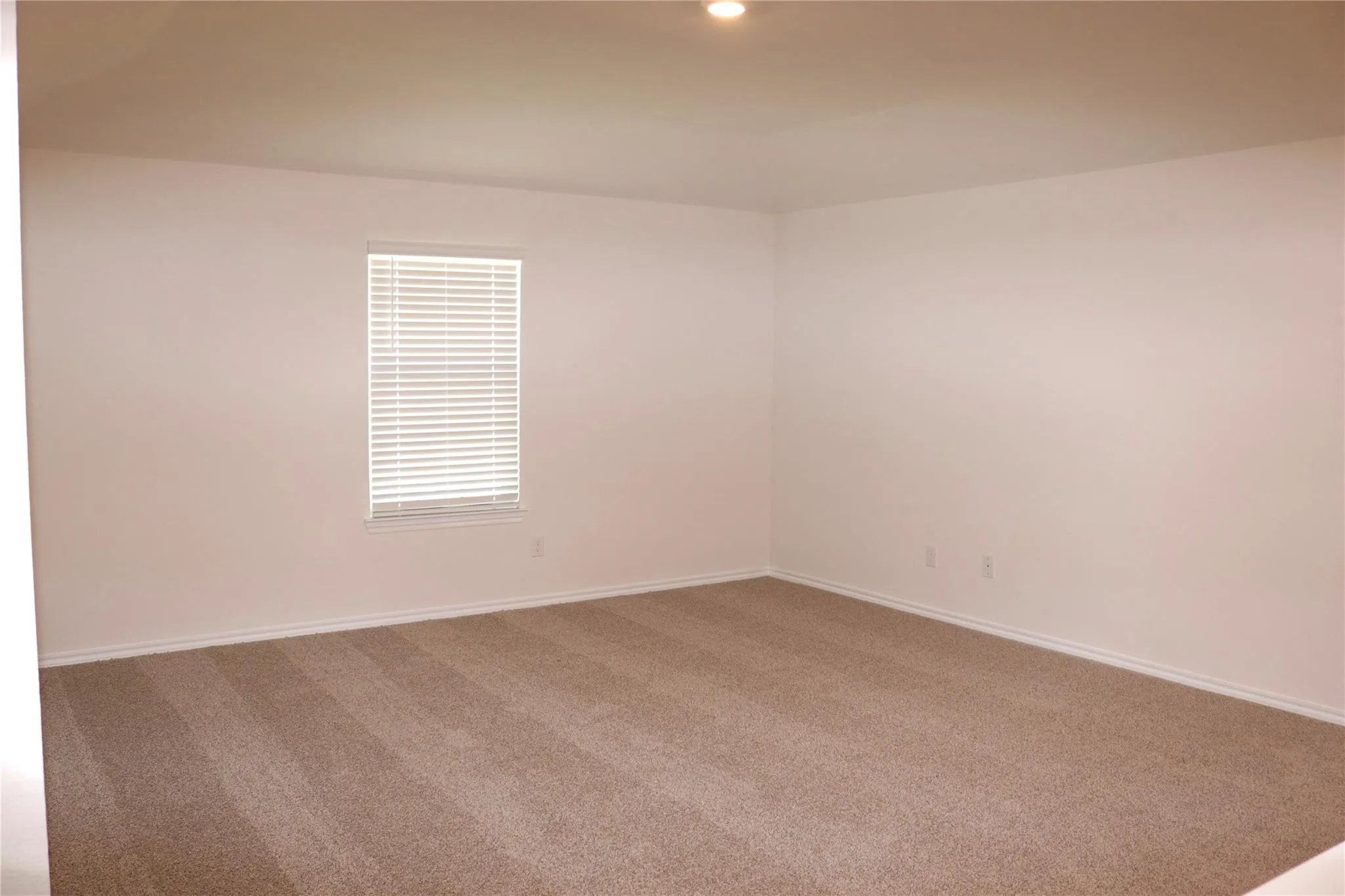 Recessed ceiling lighting, neutral carpet flooring, and a window with horizontal blinds
