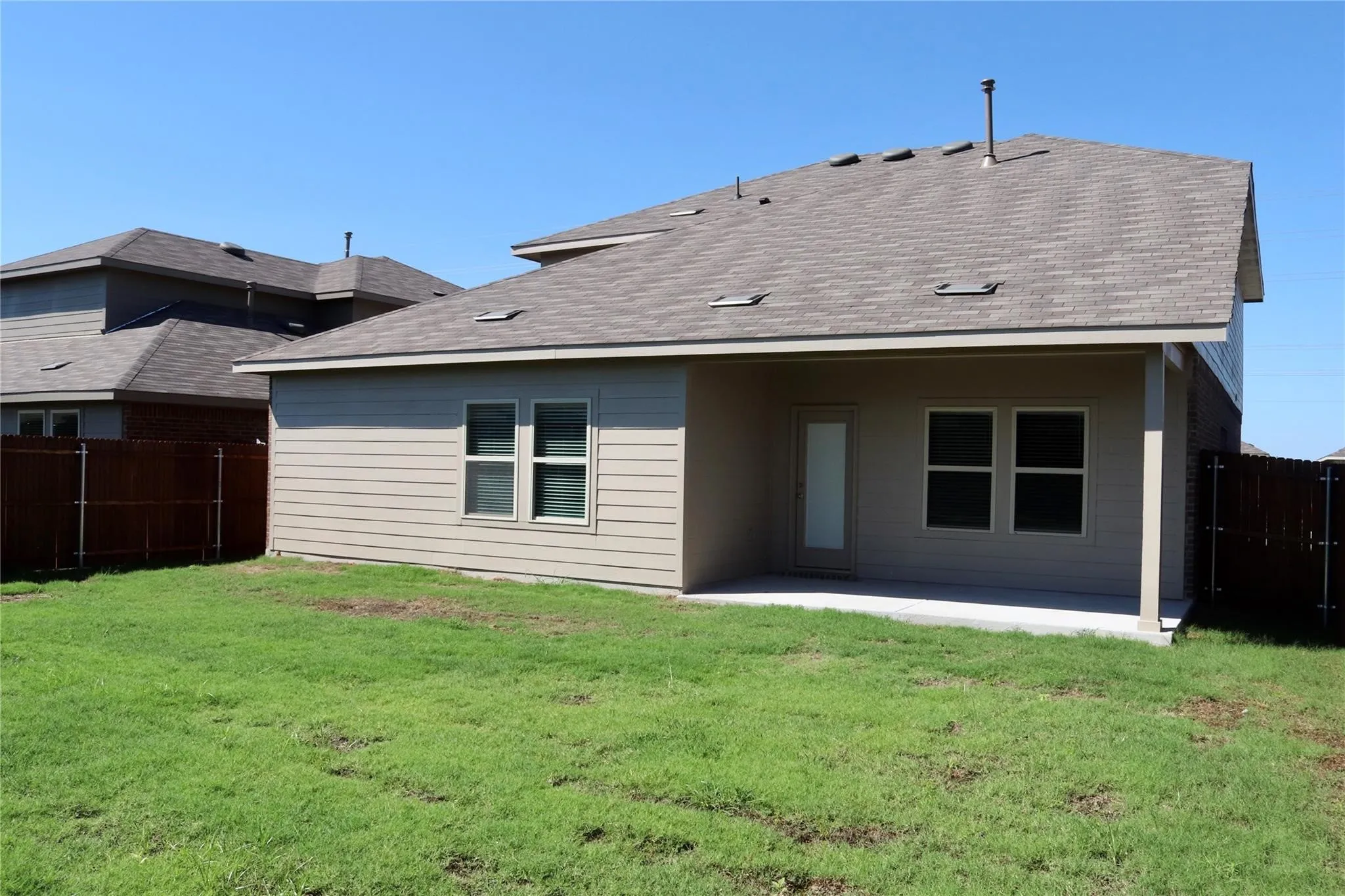Expansive backyard with a covered patio, tan siding, and a wooden privacy fence