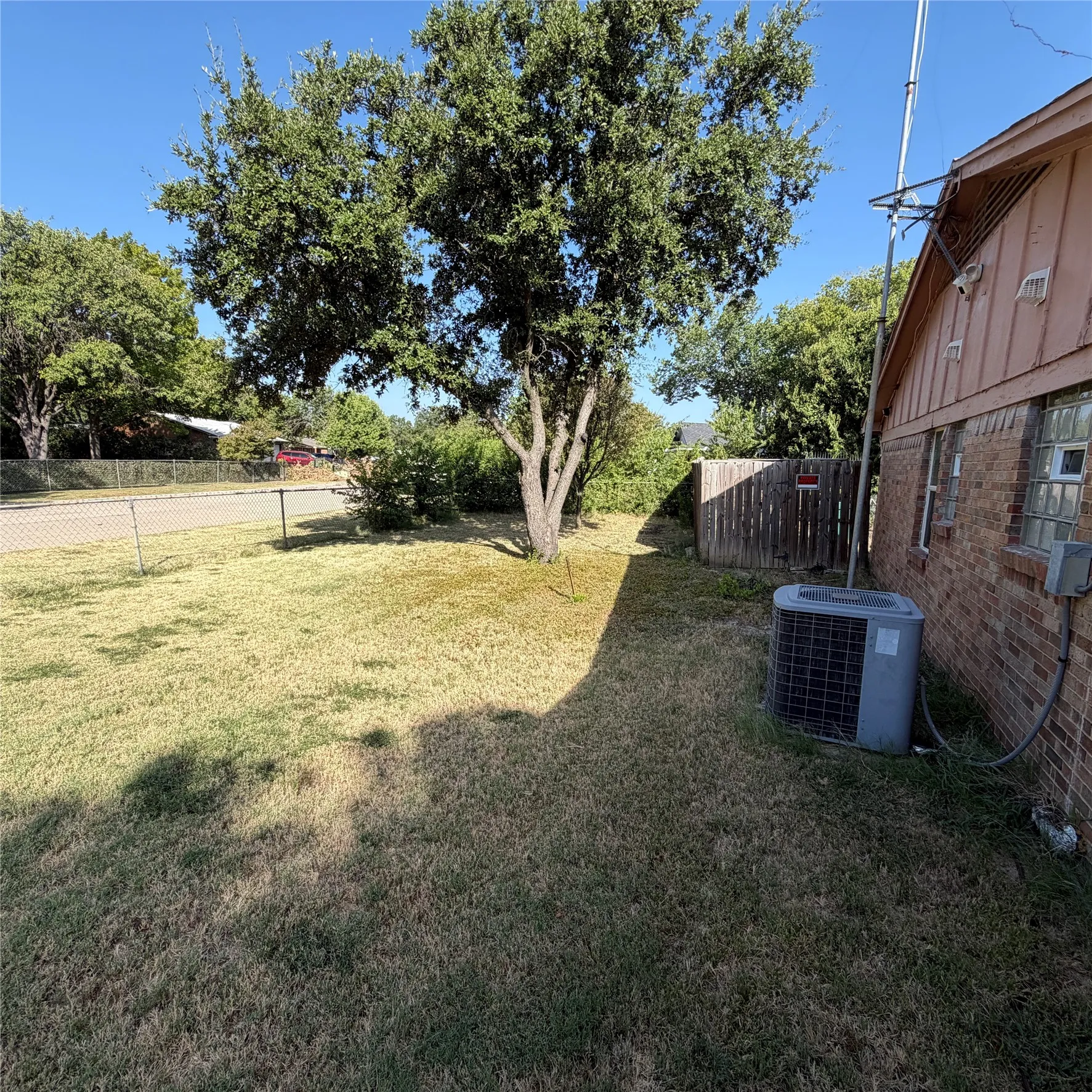 Expansive side yard featuring a mature tree, chain-link fencing, and a wooden privacy fence