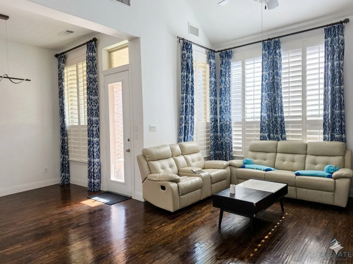 Vaulted ceiling, dark wood-finish flooring, multiple windows with plantation shutters, an exterior door with frosted glass, and transom window