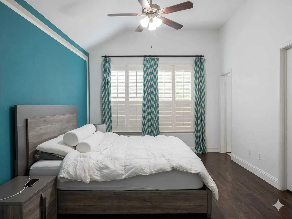 Vaulted ceiling with a ceiling fan, wood-finish flooring, plantation shutters, and a prominent accent wall