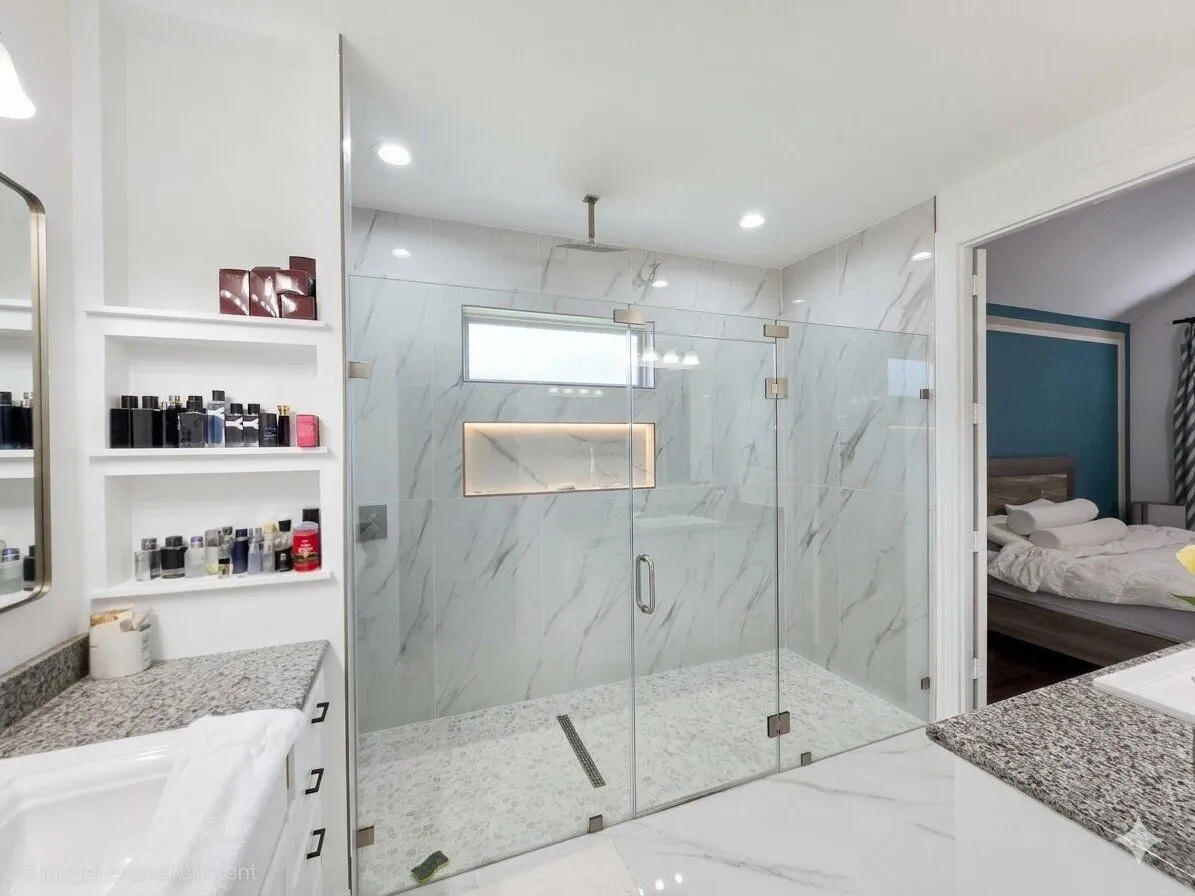 Spacious walk-in shower with clear glass enclosure, marble-style tile, and recessed niche with accent lighting