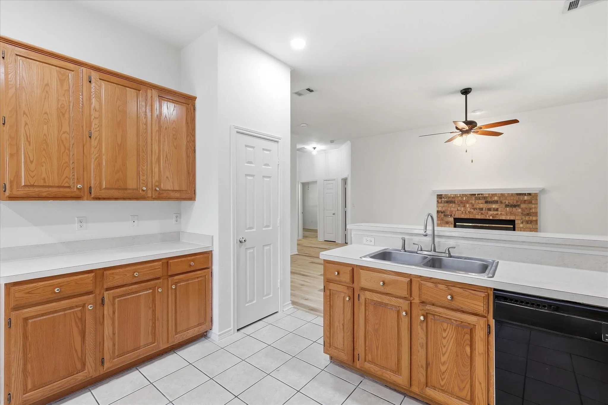 Kitchen featuring wood cabinetry, white tile flooring, stainless steel double basin sink, dishwasher, and white countertops