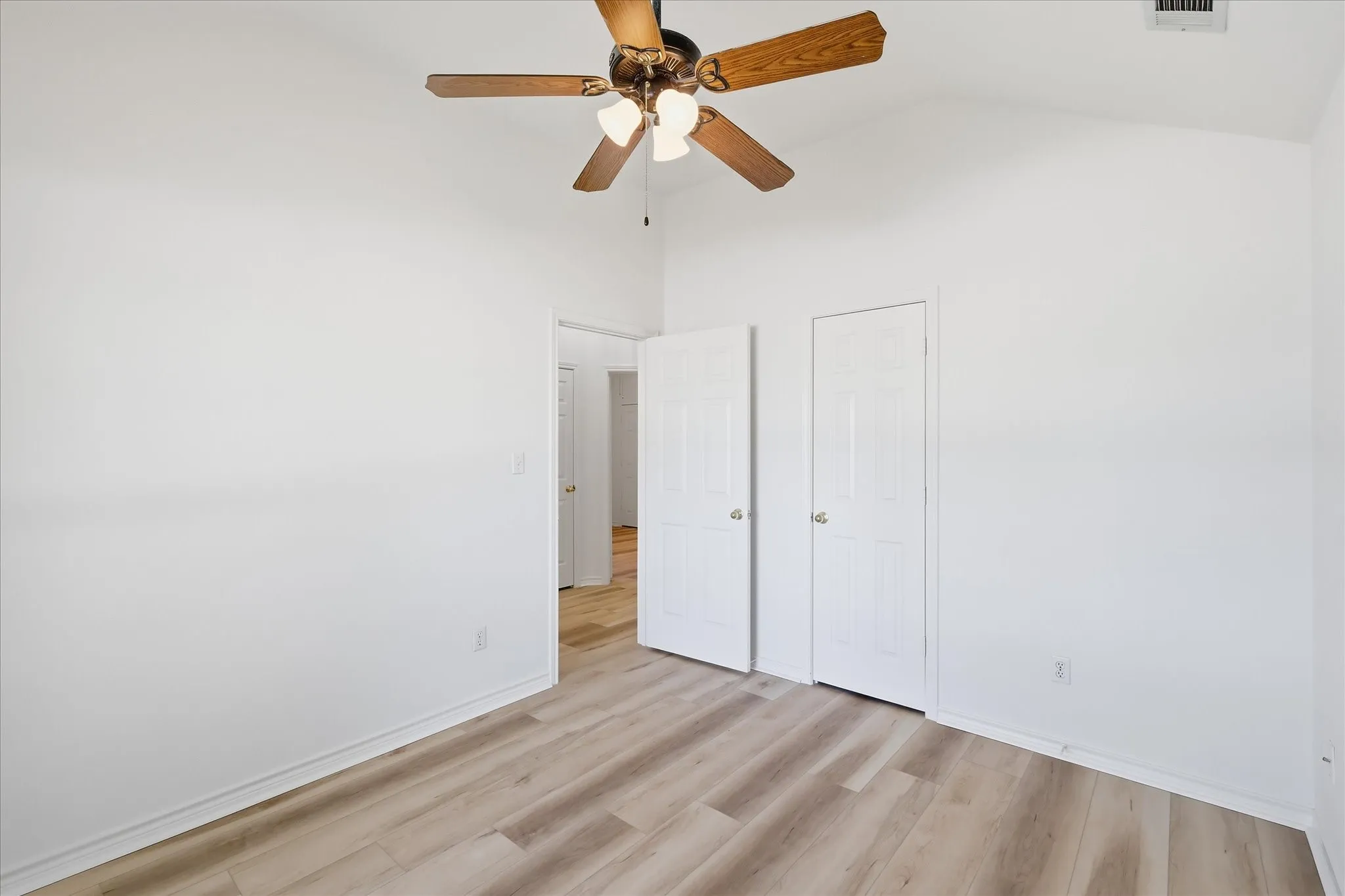 Vaulted ceiling with a wood-finish ceiling fan, wood-finish flooring, and white paneled doors