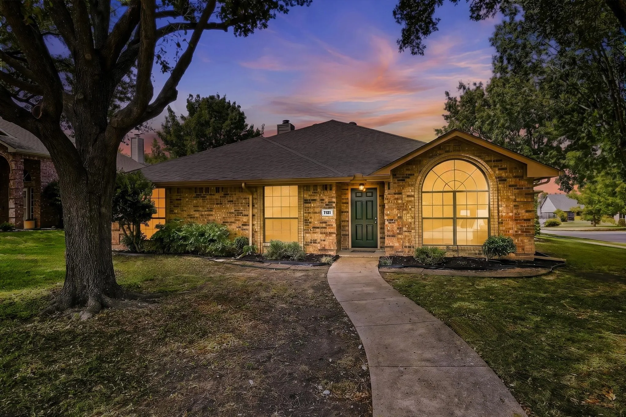 Brick exterior with an arched window, dark roof, dark paneled entry door, and a curved concrete walkway