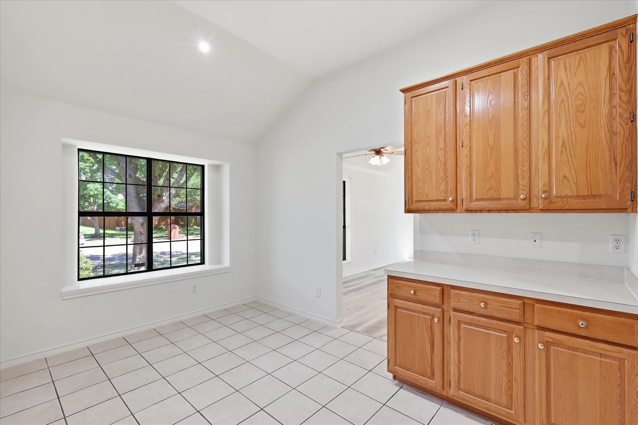 Vaulted ceiling, grid-pattern window, white tile flooring, wood-finish cabinetry, and solid surface countertop