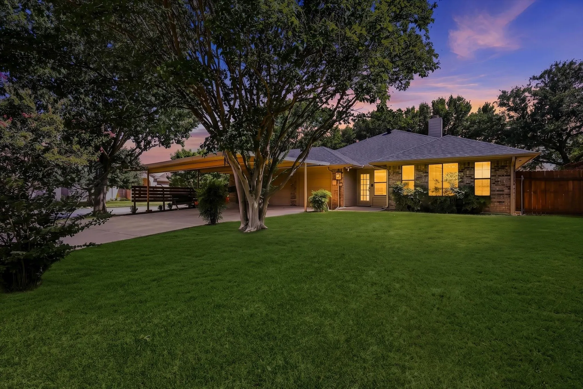 Expansive front yard with a manicured lawn, mature trees, and a concrete driveway