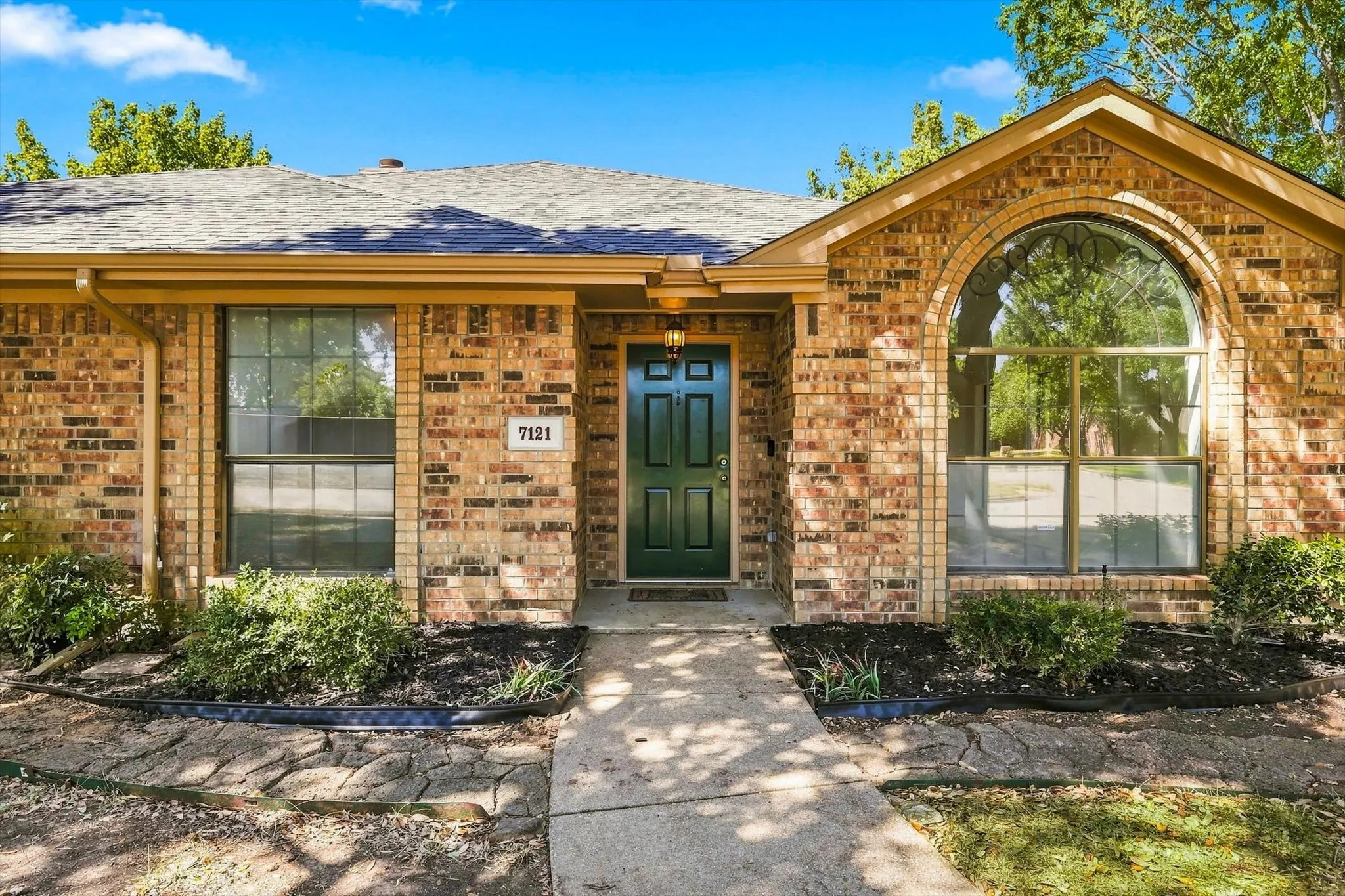 Charming brick home featuring a welcoming front entrance with arched architectural detailing, dark green entry door, and paired windows with clean sightlines