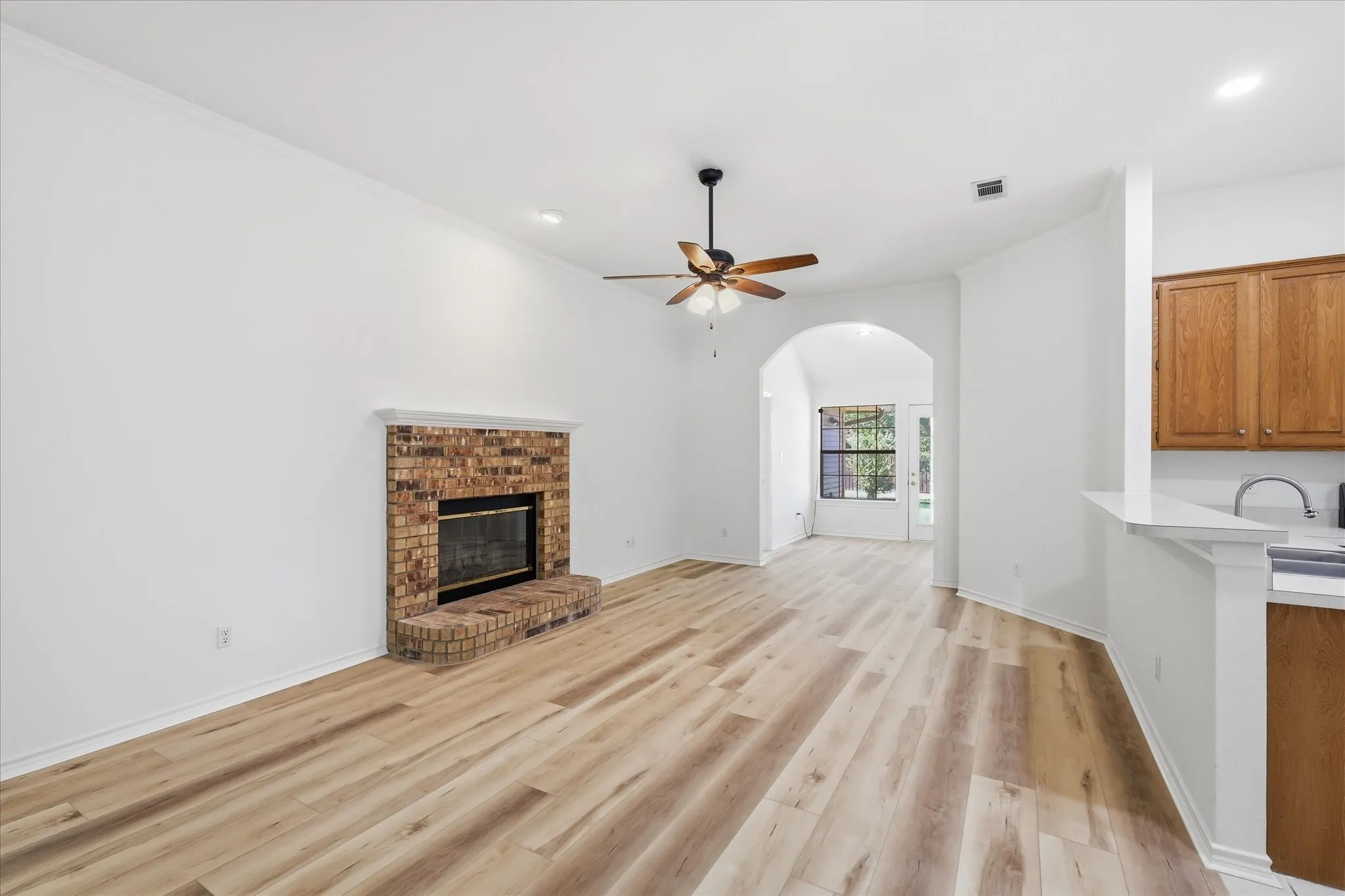 Spacious living area featuring wood-finish flooring, a brick fireplace with a mantel, a ceiling fan, and an arched doorway